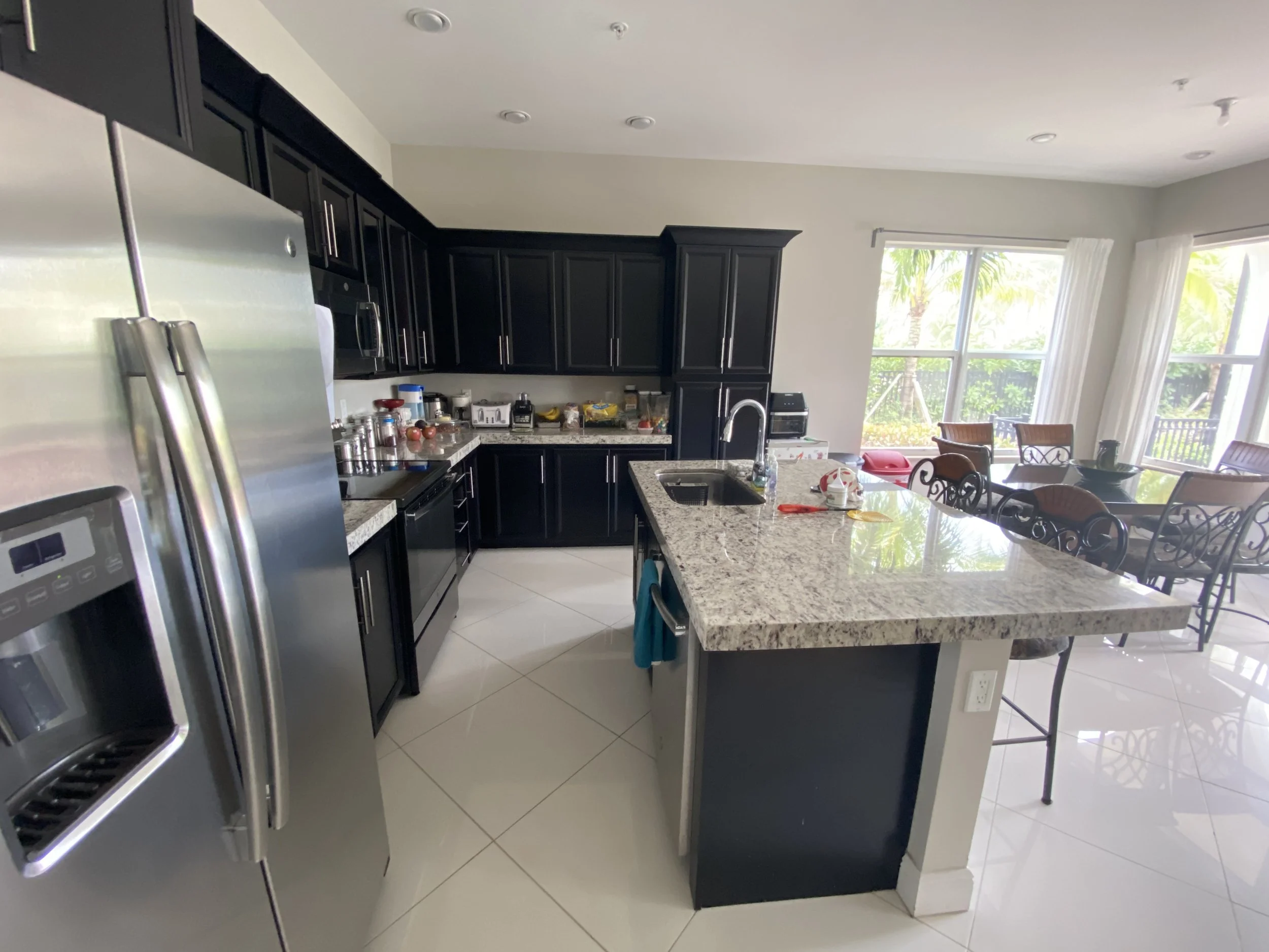 Modern kitchen with black cabinets, stainless steel refrigerator, granite countertops, and large window.