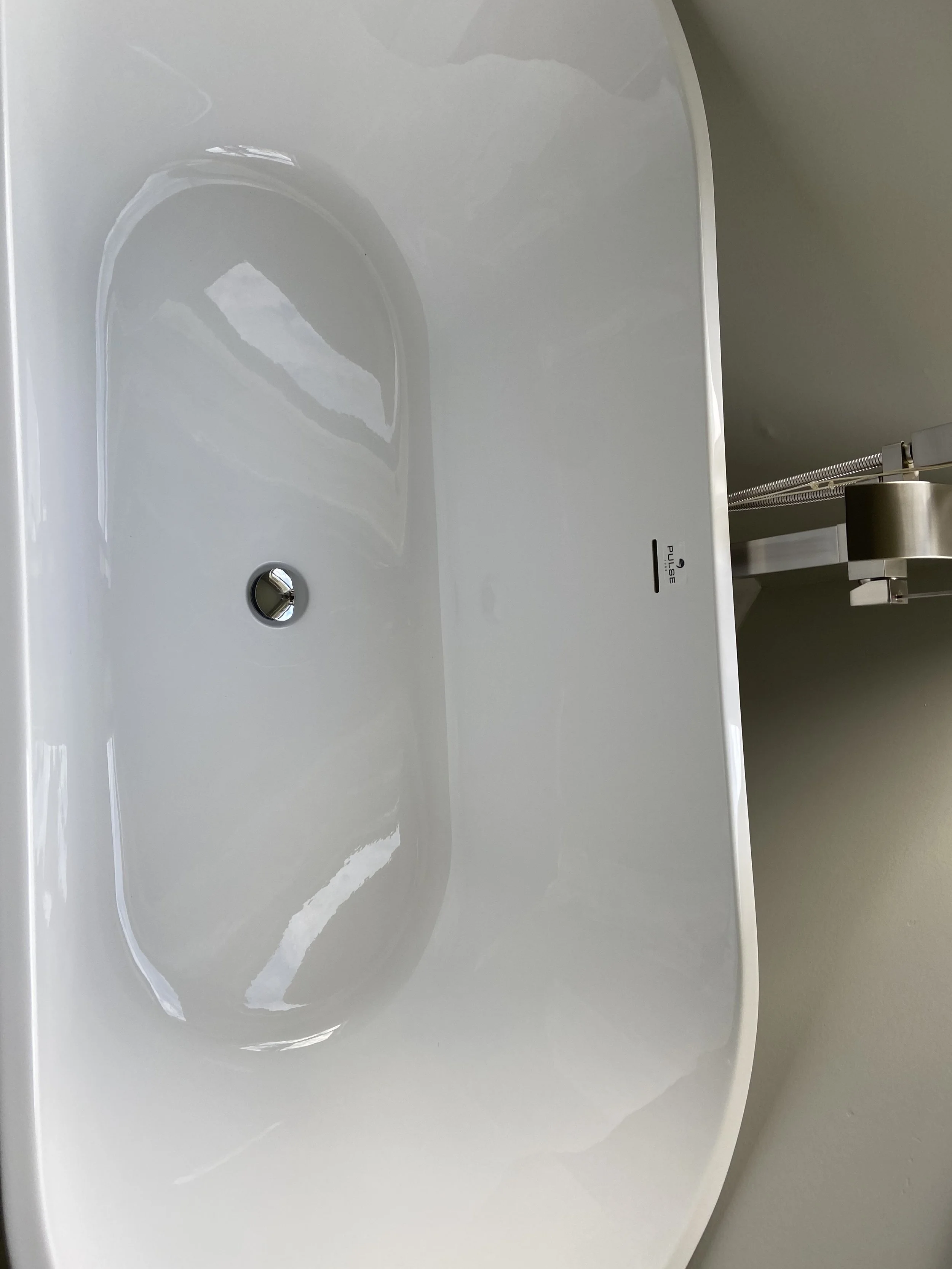 Empty white bathtub with a drain and overflow, silver faucet, and a push button control on the side
