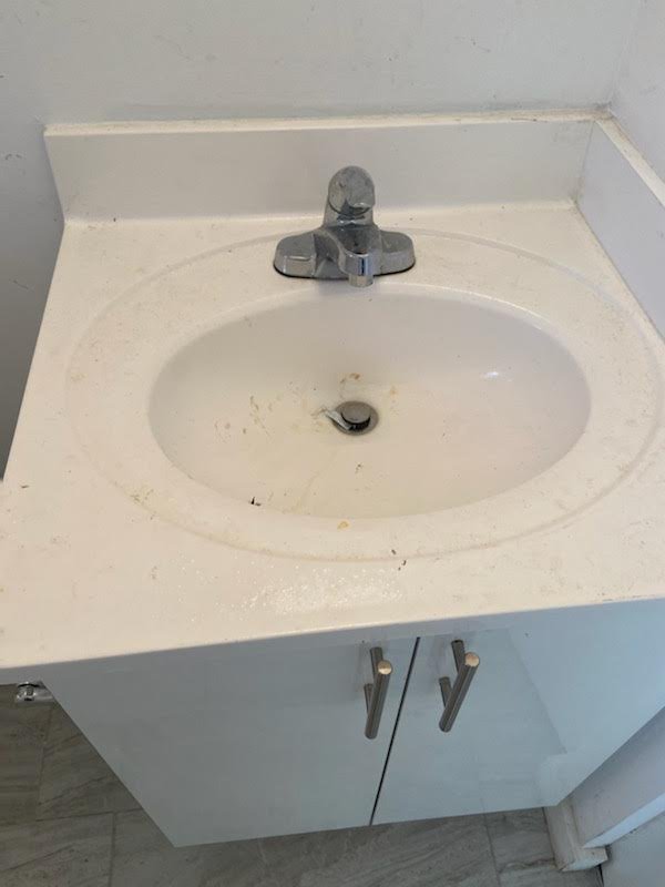 Bathroom sink with a silver faucet, surrounded by a white countertop and cabinet, with minor stains and dirt inside the sink basin.