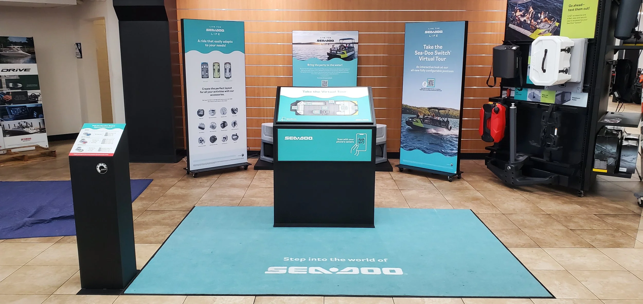 Indoor display area showcasing Sea-Doo watercraft and accessories with promotional posters and a touch screen for virtual tour experience.