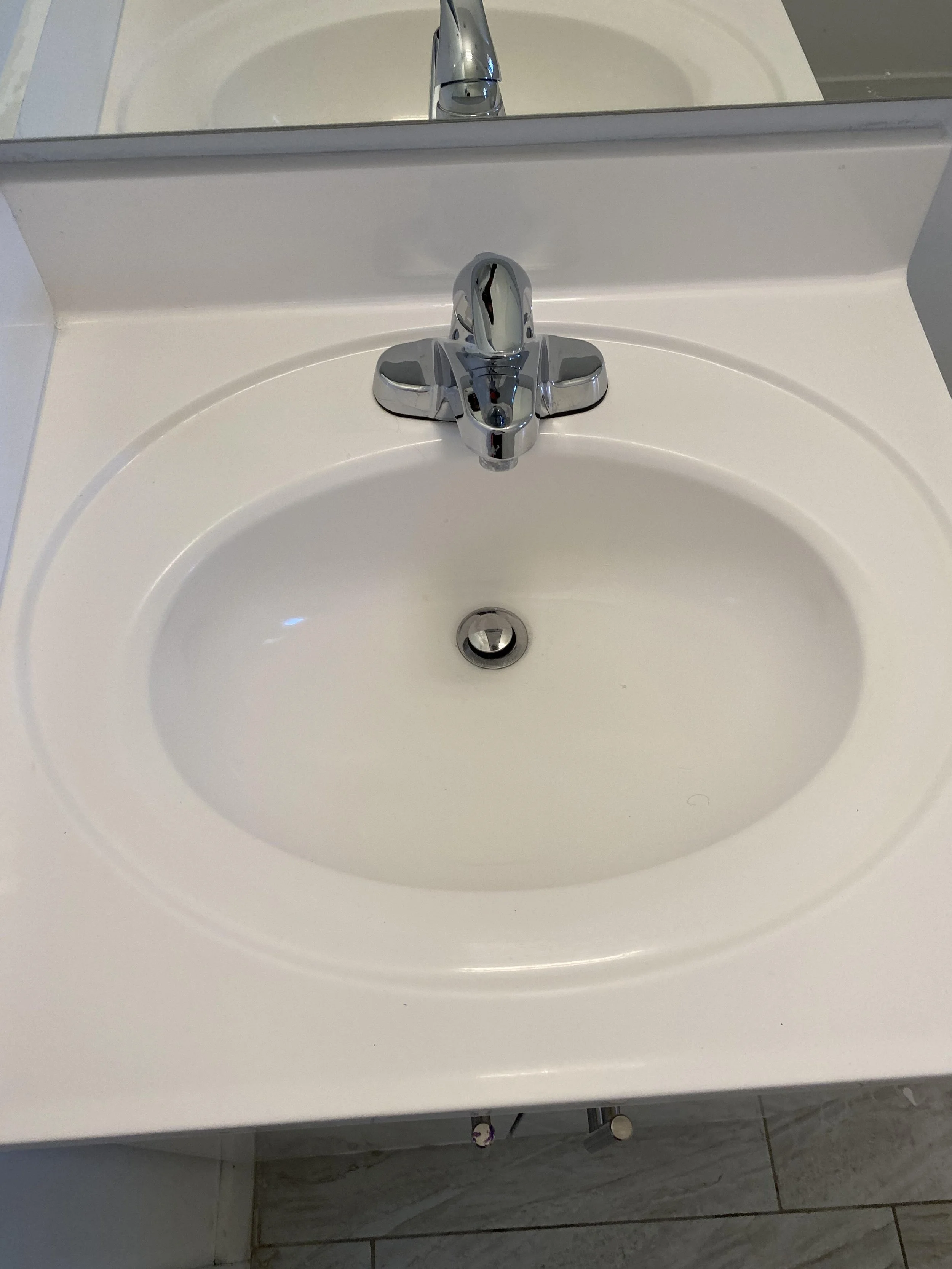 A white bathroom sink with a chrome faucet, a mirror above it, and a tiled floor.
