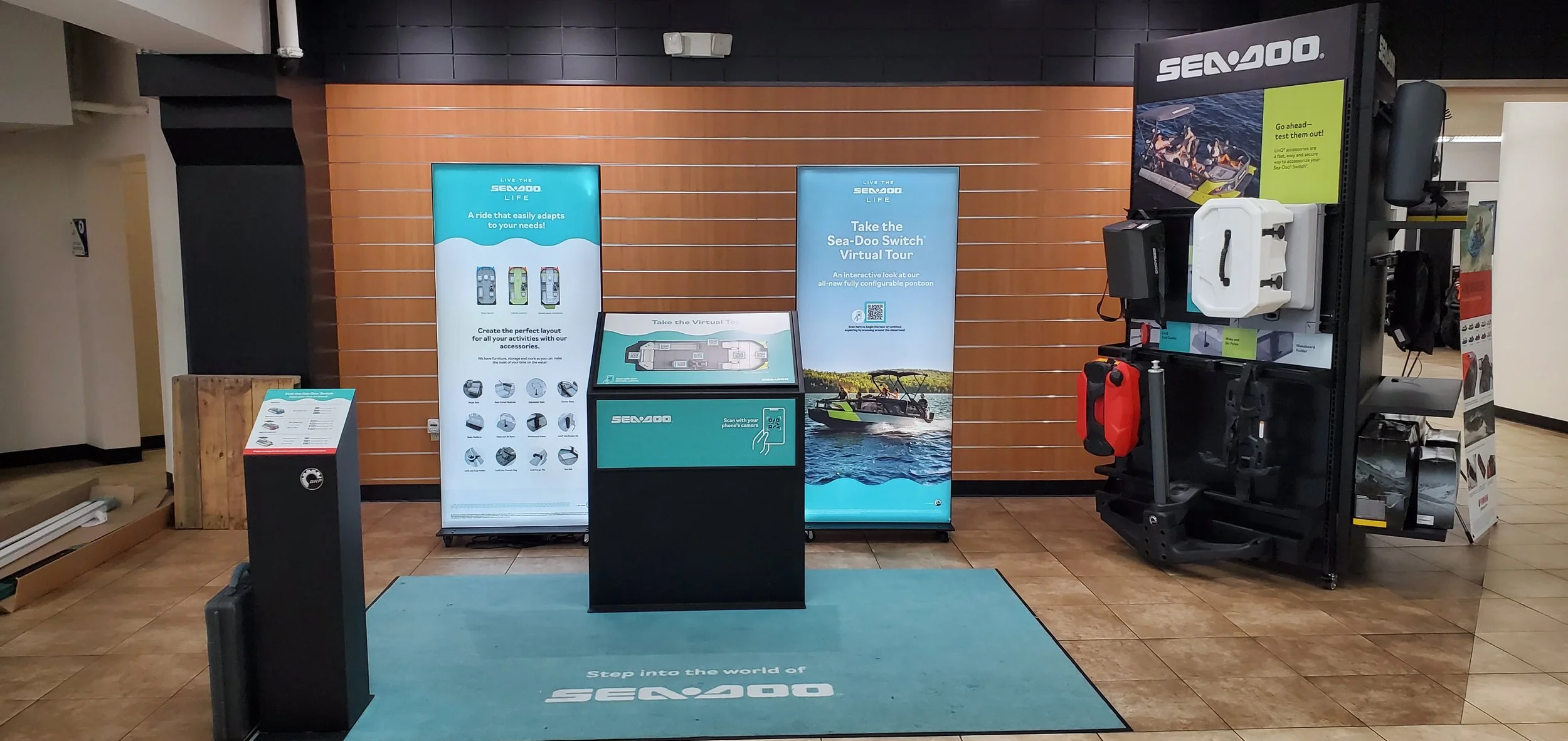Display at an outdoor adventure store showcasing Sea-Doo watercraft products, featuring informational banners, digital screens, and safety gear.