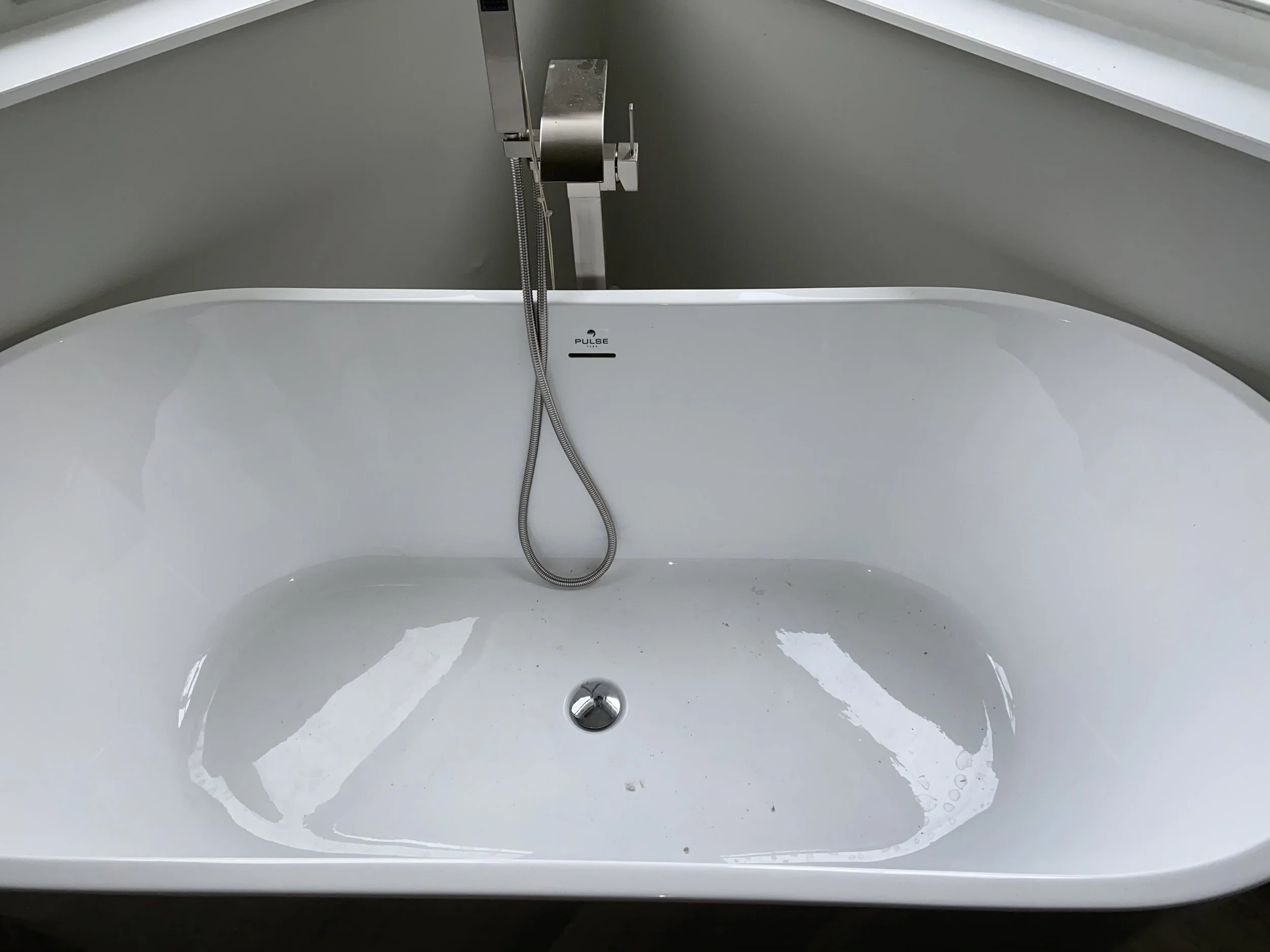 Empty white bathtub with a silver faucet and a handheld showerhead, situated beneath a window.