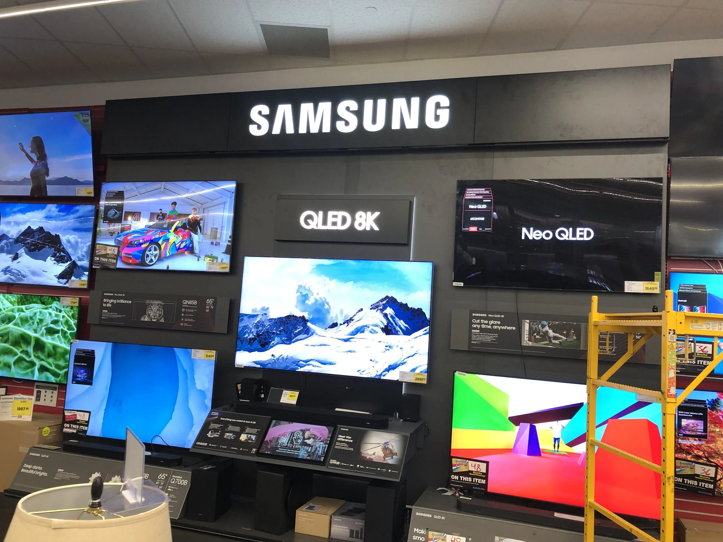 Display of multiple flat-screen televisions at an electronics store, with Samsung branding and various models displayed.