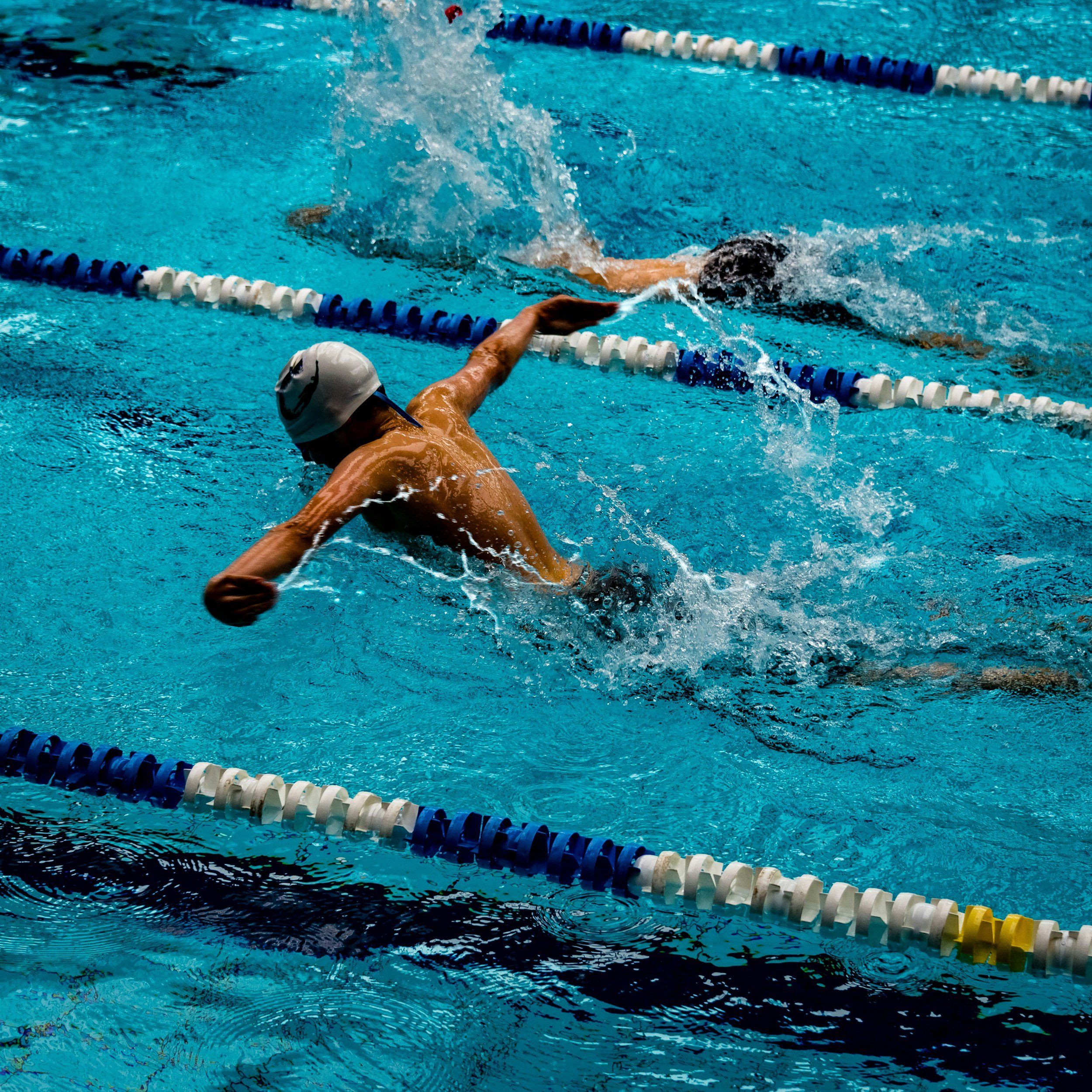Swimmer performing overhead stroke in pool, representing repetitive motion and overuse injuries that can cause shoulder pain treated with massage therapy in Charlotte NC