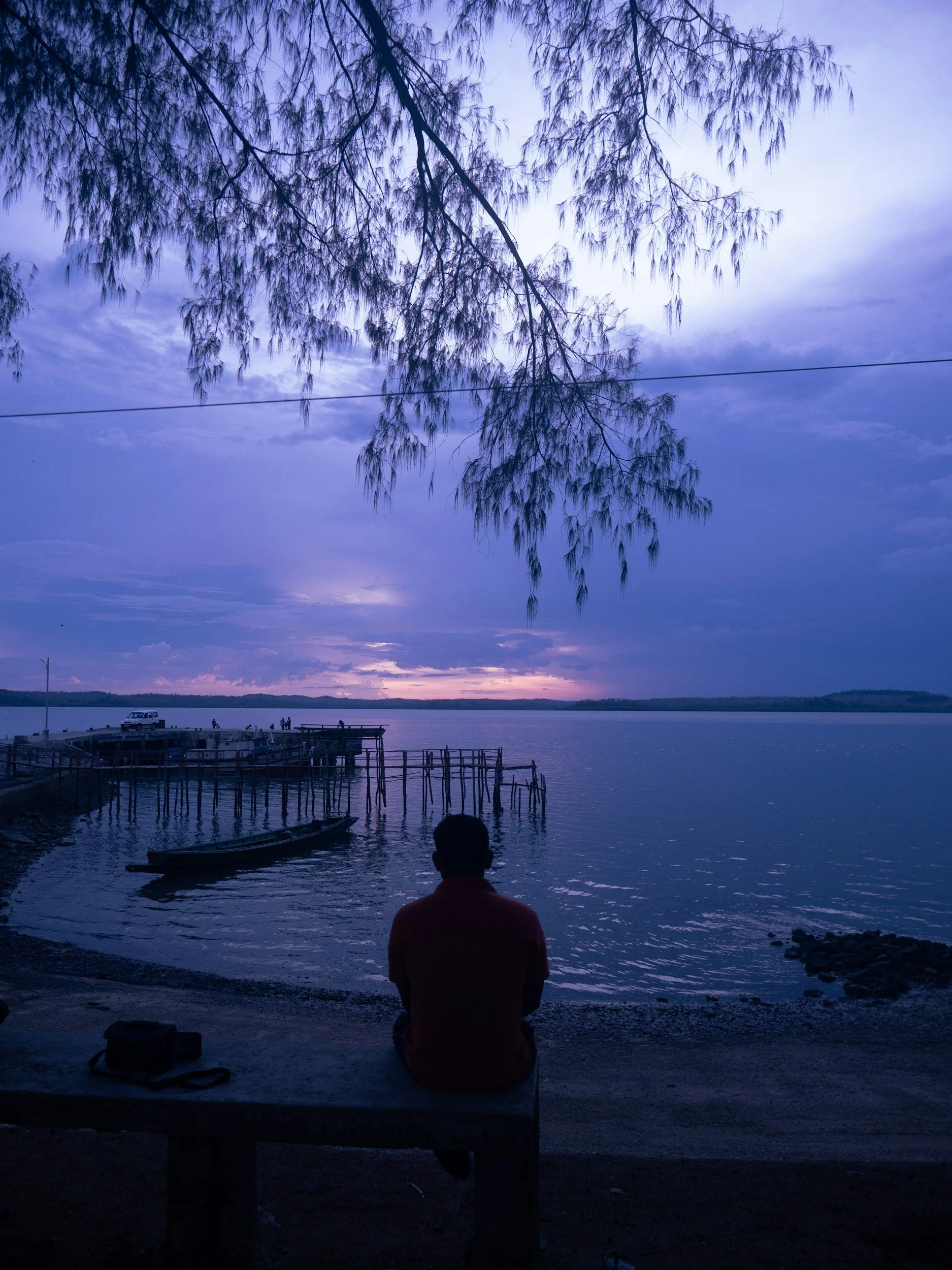 Person sitting quietly beside a lake at sunset, reflecting during a period of grief, loss, or major life transition while seeking peace and emotional support.