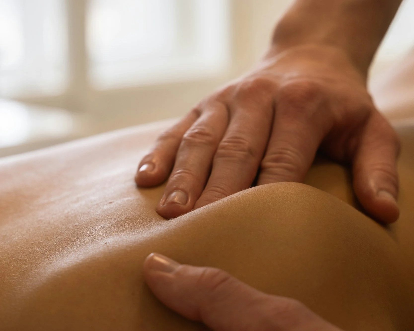 Targeted neuromuscular therapy being applied to the shoulder blade of a client on a therapy table.