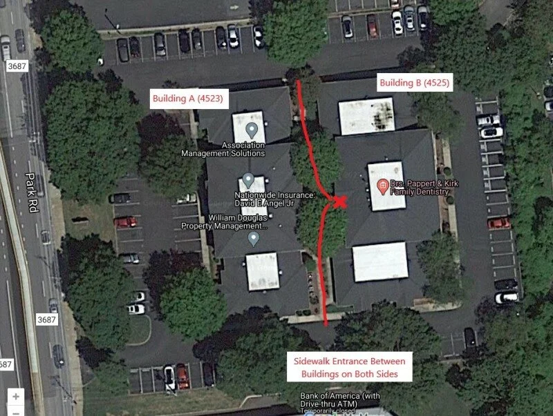 Aerial view of a commercial complex showing two buildings labeled A and B, with a red line and arrow indicating a sidewalk entrance between the buildings on both sides. Surrounding parking lots and trees are visible.