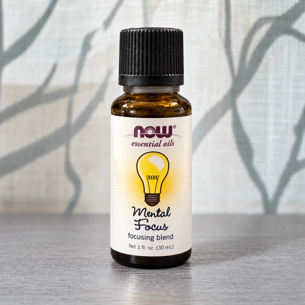 NOW Mental Focus essential oil blend bottle against a softly lit curtain