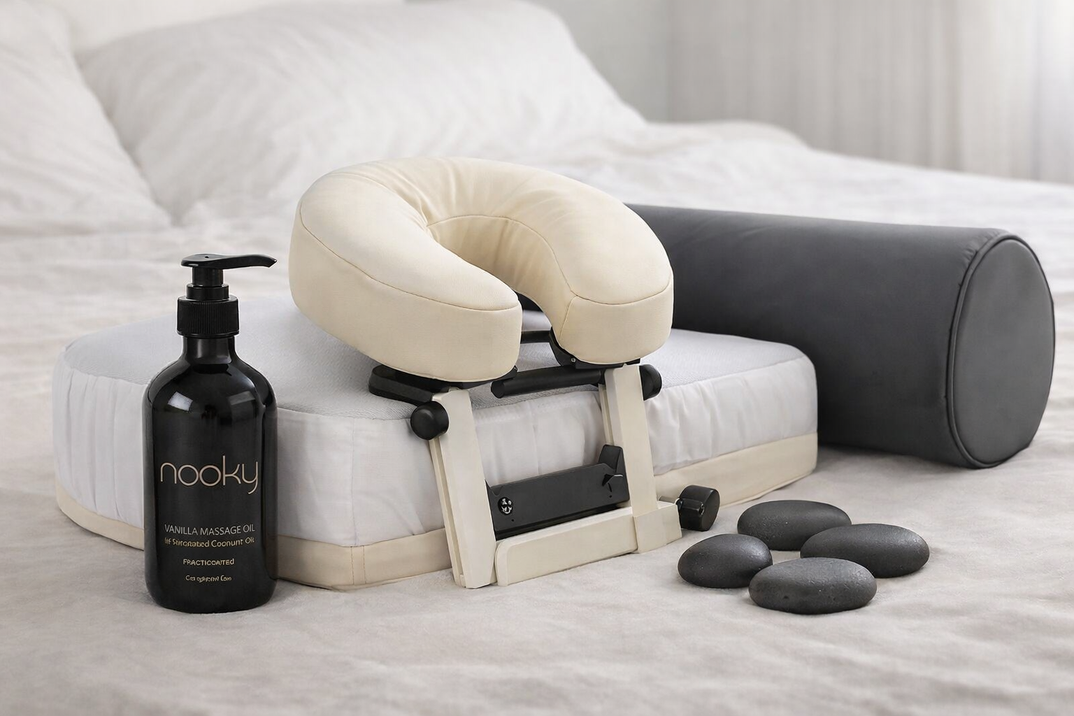 Bed-top massage setup with face cradle, bolster pillow, massage oil, and warm stones for partner massage at home