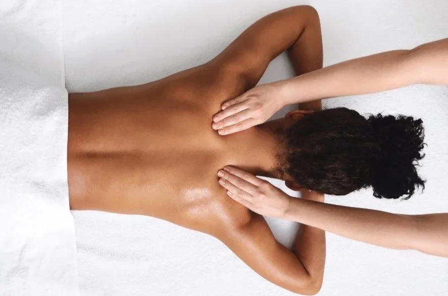 Massage therapist applying broad, flowing pressure to the upper back to support muscle recovery and overall relaxation