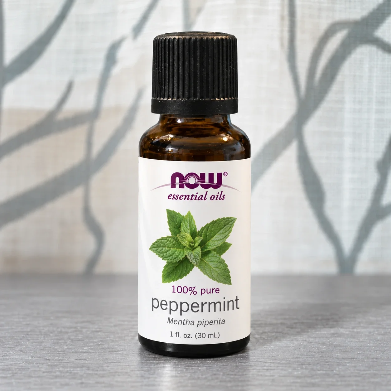 NOW peppermint essential oil bottle against a softly lit curtain