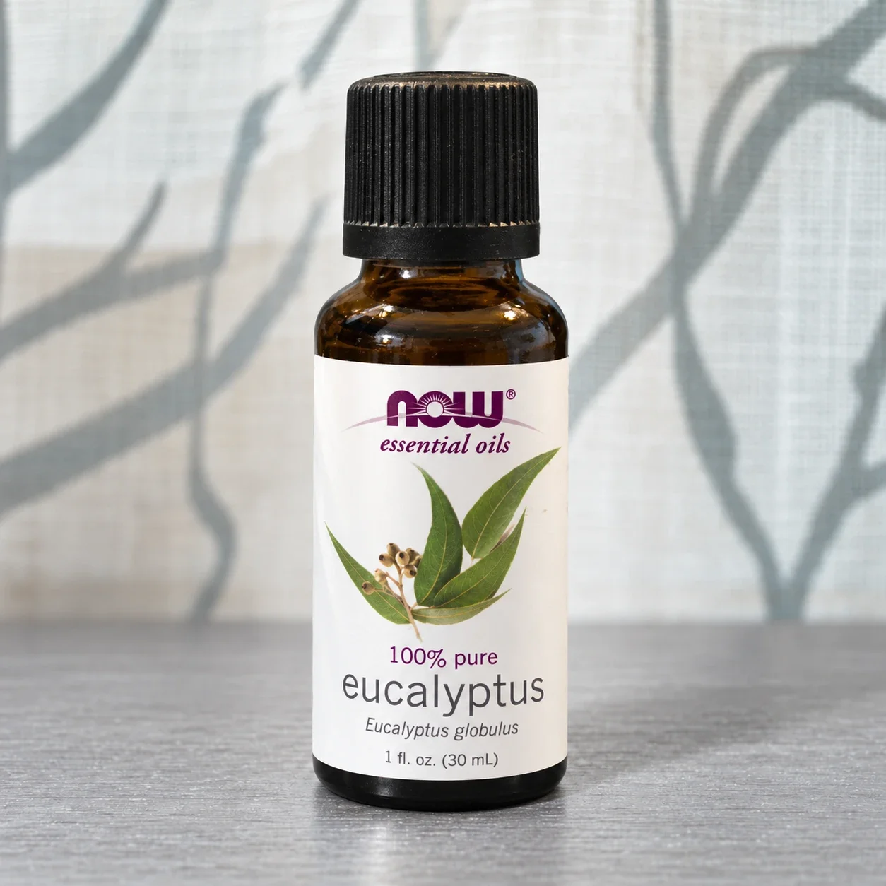 NOW eucalyptus essential oil bottle against a softly lit curtain