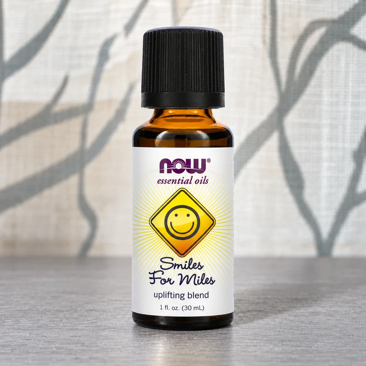 NOW Smiles for Miles essential oil blend bottle against a softly lit curtain