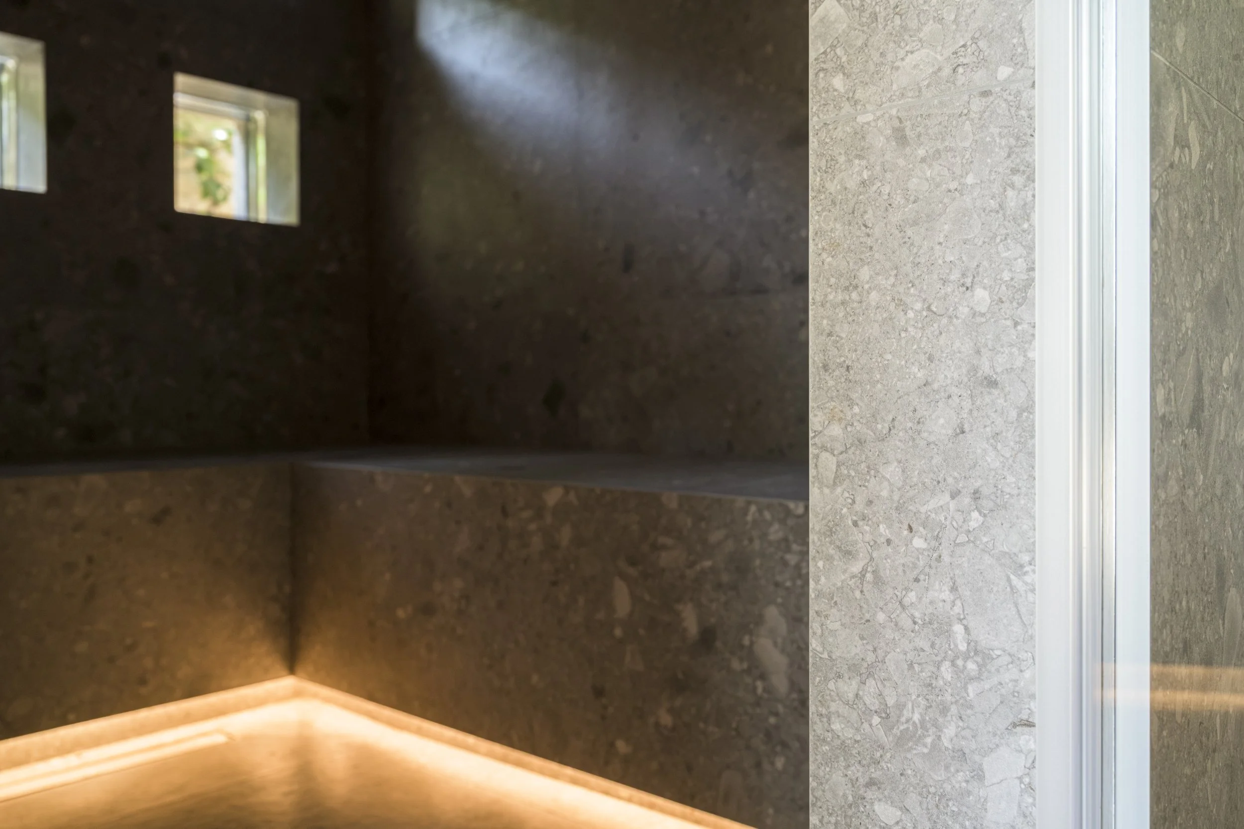 Détail de la porte du hammam : un profilé fin en aluminium, encastré dans l'ébrasement carrelé, marque le seuil entre la circulation et le hammam sans interrompre le revêtement.