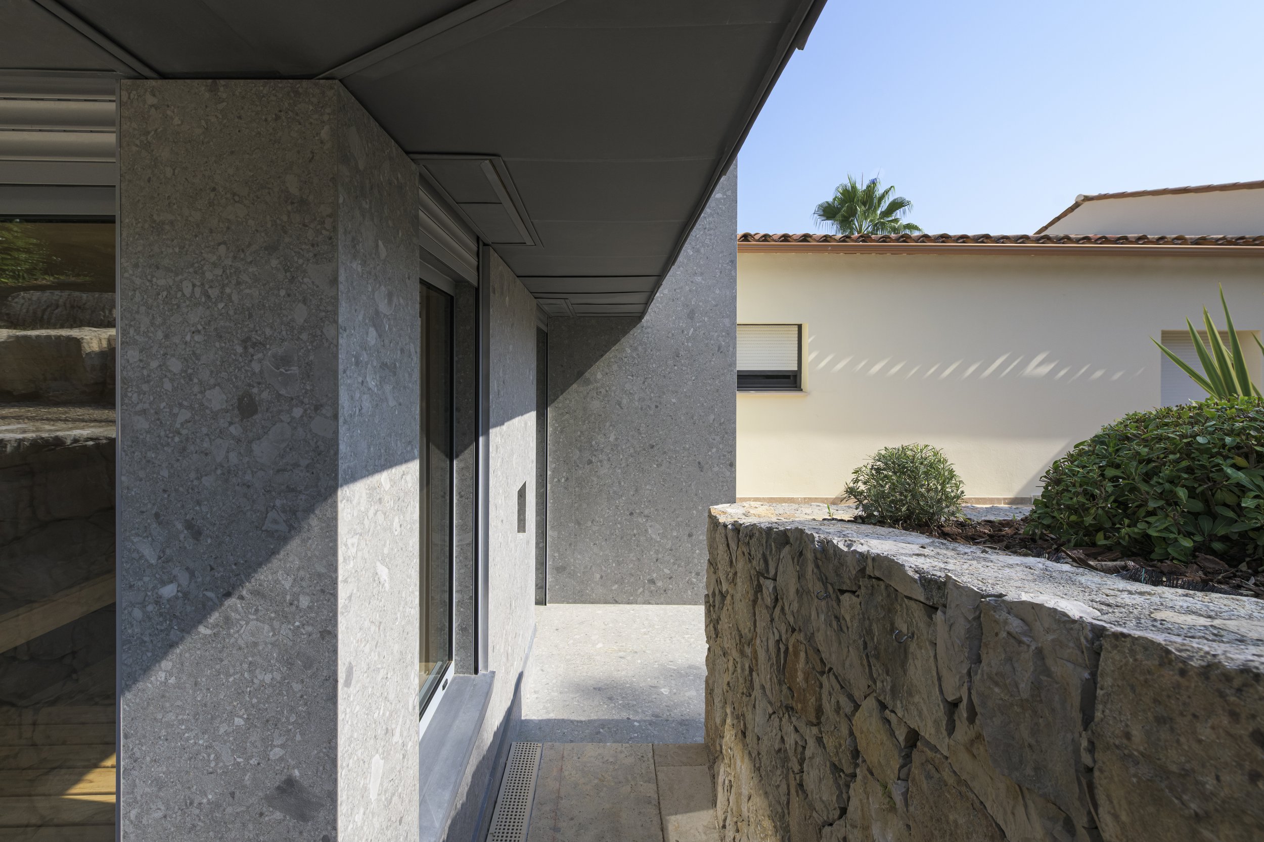 Sol et murs de l'extension dans le même revêtement minéral, le mur en moellons conservé et l'enduit de la villa existante : trois strates réunies dans une même vue.
