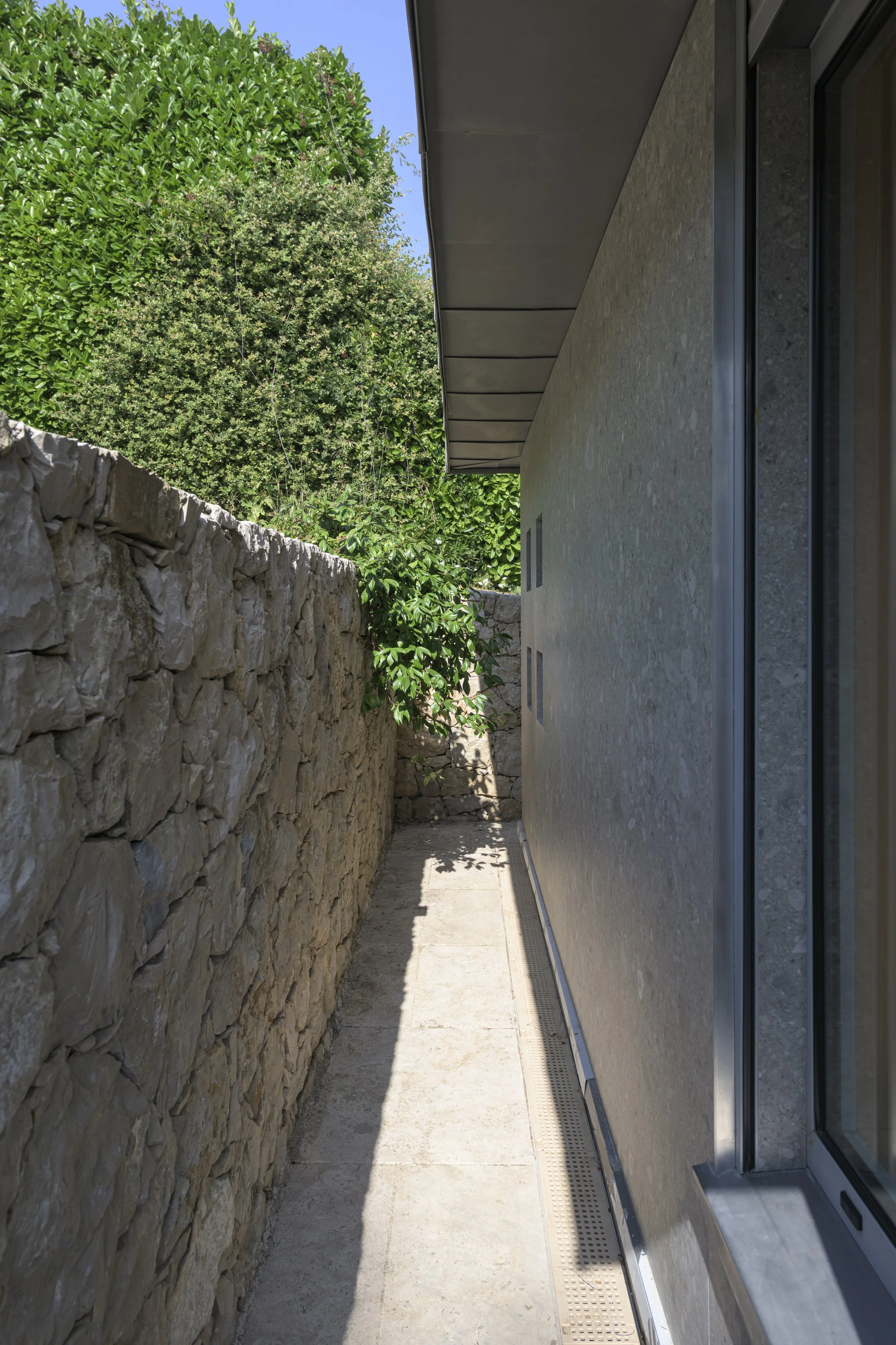 L'extension s'insère dans la terrasse en laissant un passage étroit le long du mur en moellons existant : le nouveau et l'ancien se font face sans se toucher.