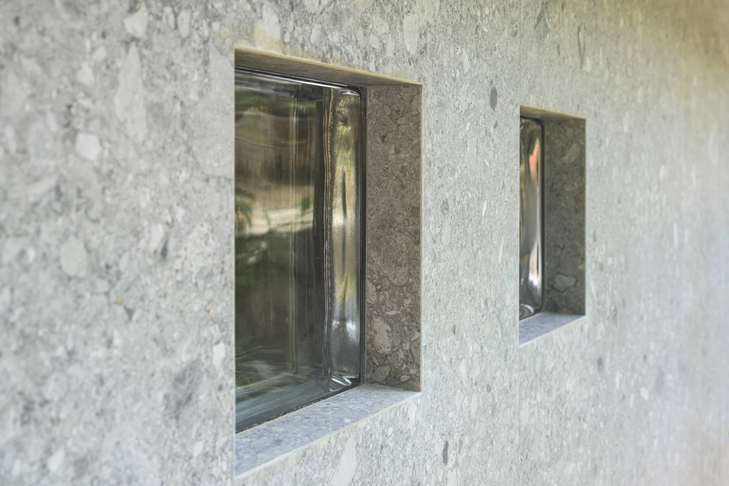 Détail d'exécution : le carrelage se retourne dans l'épaisseur du mur et encadre les pavés de verre, sans profilé ni joint apparent.