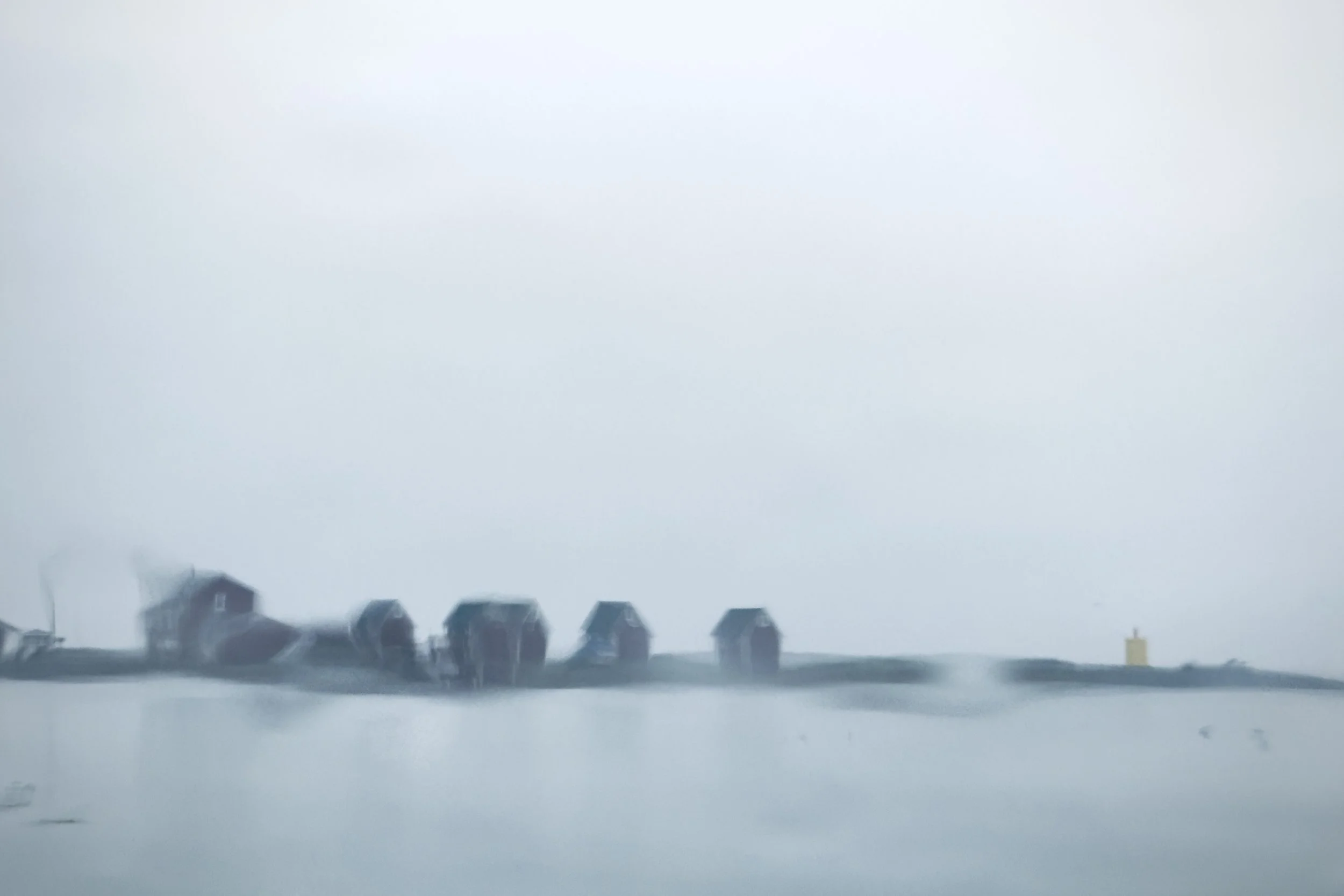 Abstract view of five houses and the sea in Iceland, seen through a rain-covered car window.