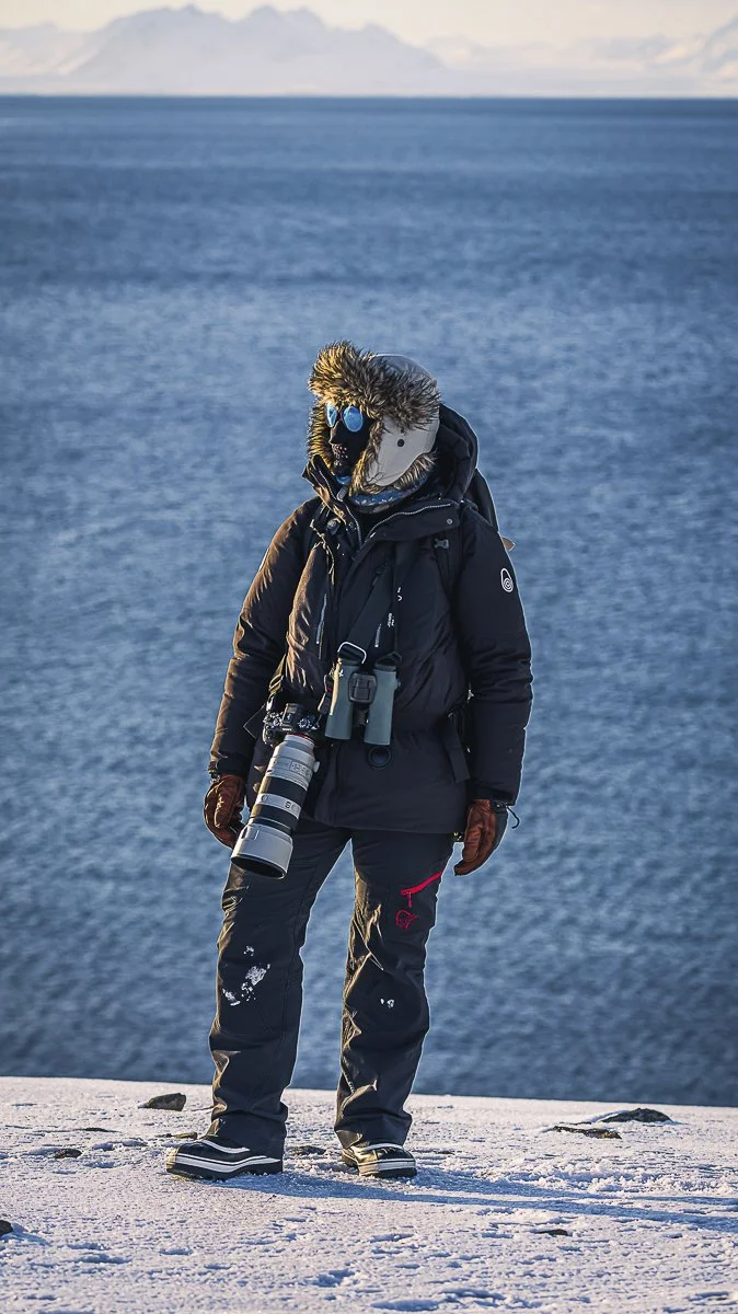 Photographer standing outdoors in the Arctic winter wearing full cold-weather clothing and a face protector.