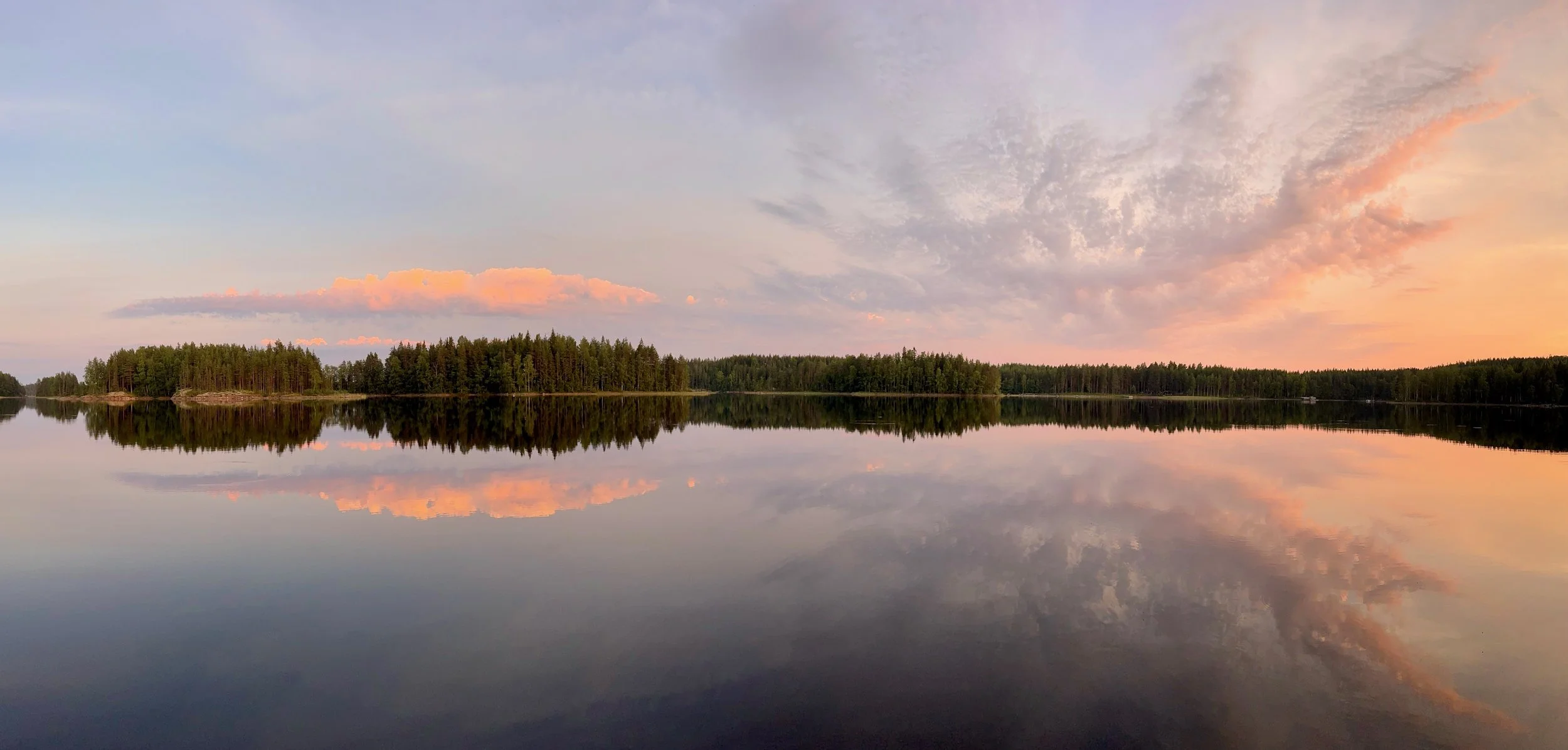 Summer landscape of Lake Saimaa in Finland, with the lake surrounded by forested shoreline, sunset