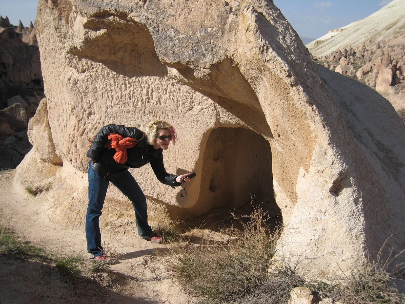 A photograph of me wearing jeans and a leather jacket, leaning over to shine a small flashlight into a cave carved into a rock formation.
