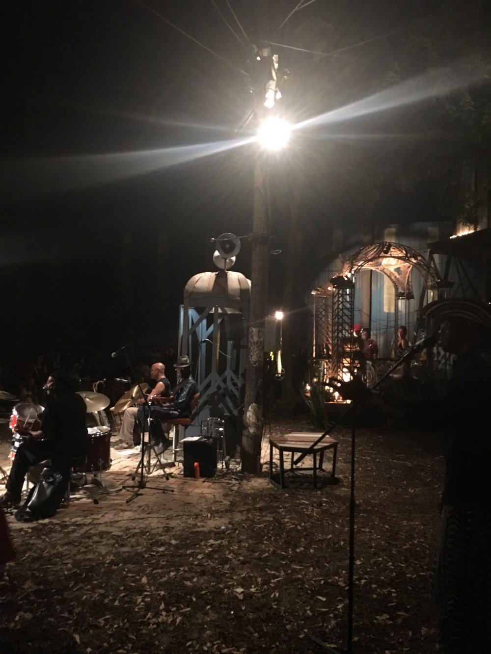 A photograph by the author of half a dozen musicians playing various instruments in spot-lit pavilions outside at night time.