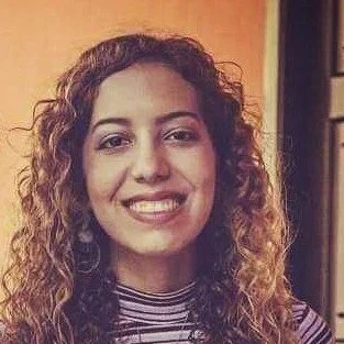 Smiling woman with curly brown hair wearing a striped shirt, looking directly at the camera.