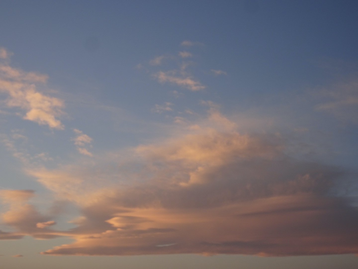 A photo of the sunset sky dominated by a large mound of soft cloud in shades of pink, lilac, and violet.
