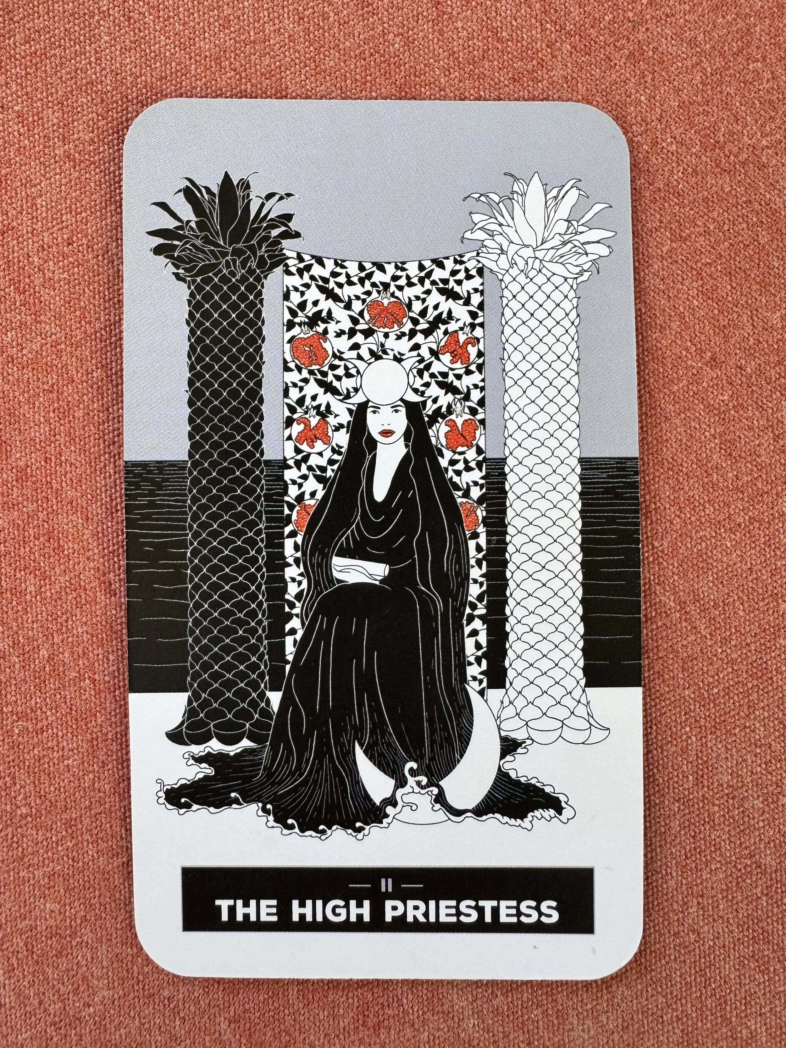 Tarot card depicting "The High Priestess" with a woman in a black robe and veil seated between two ornate pillars and a tapestry with pomegranates.