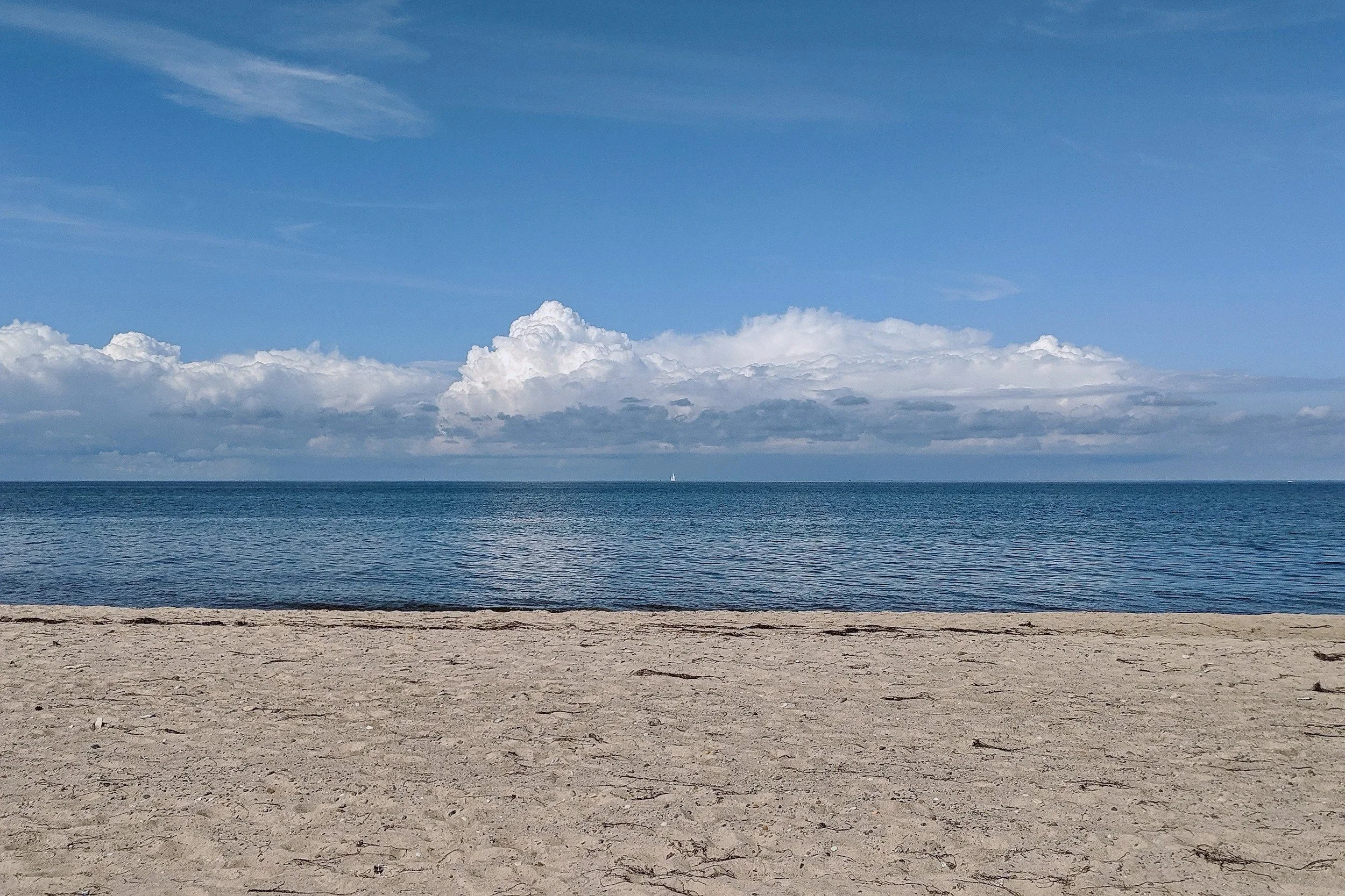 A sandy beach with calm ocean water and blue sky with scattered clouds.