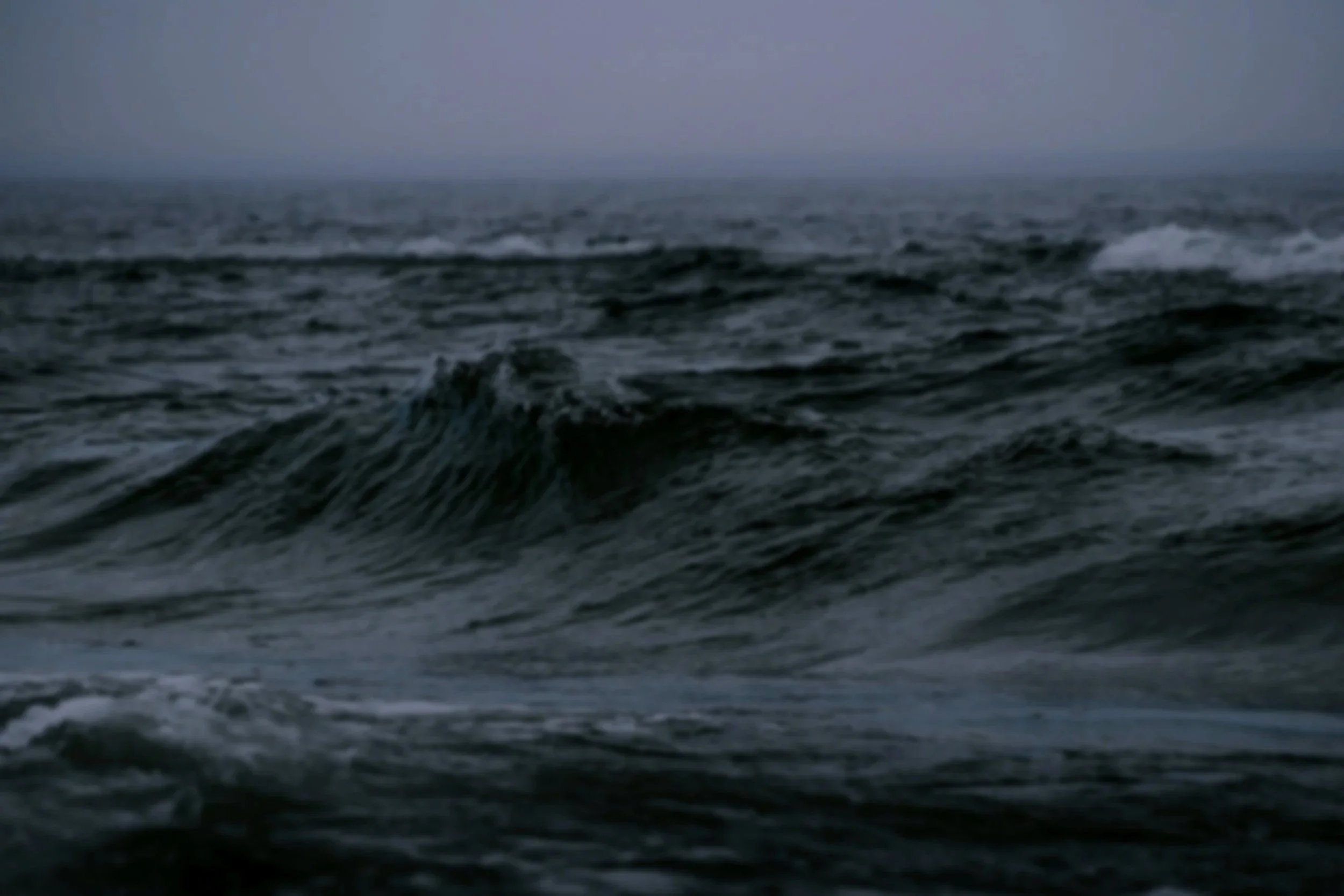 Dark ocean waves under a cloudy, overcast sky.