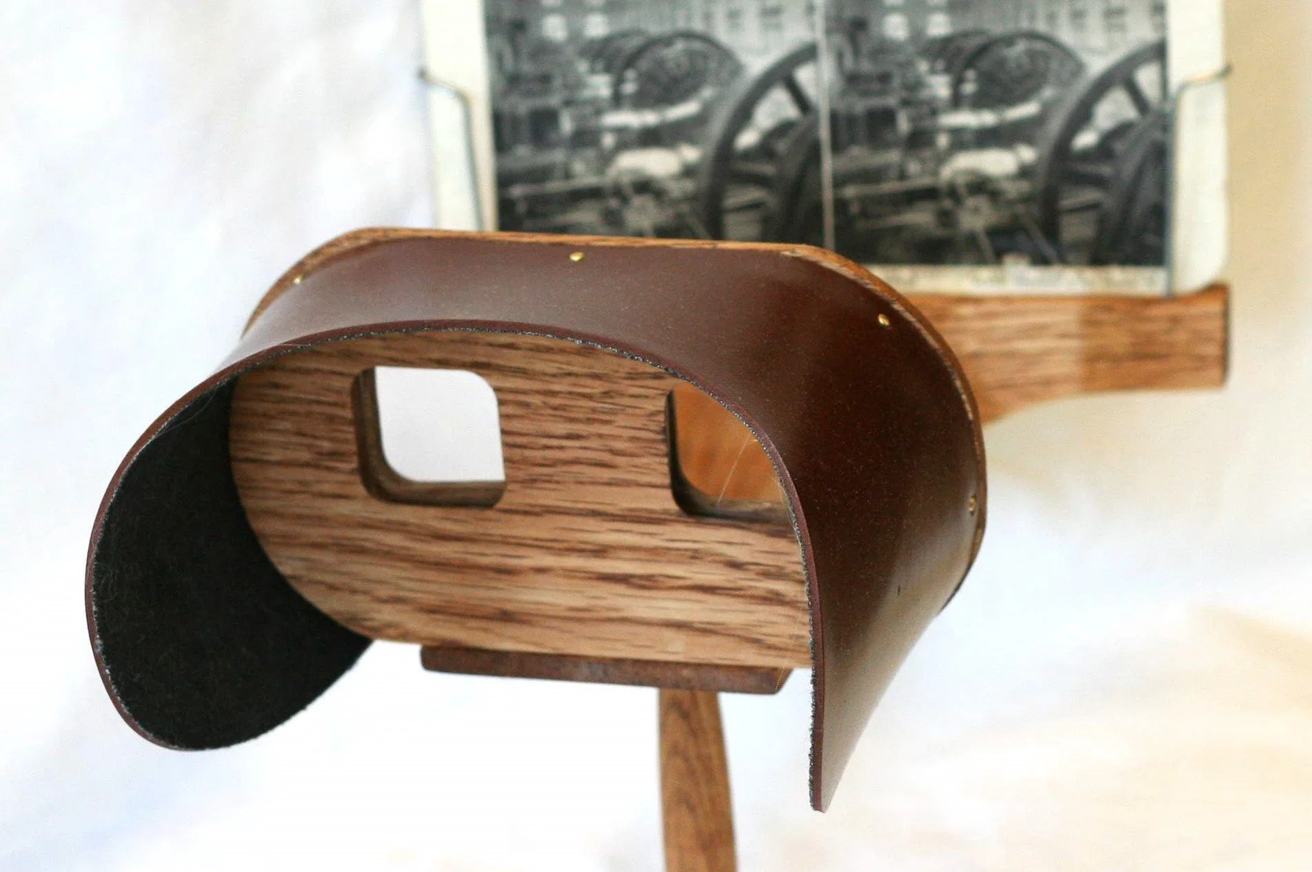 A photograph of a old fashioned wood and leather viewfinder looking toward a stereoscope photograph on the wall.