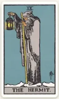 The Hermit tarot card, depicting a white-bearded, robed man standing at the edge of a cliff, holding up a lit lantern in one hand and holding a tall staff in the other.