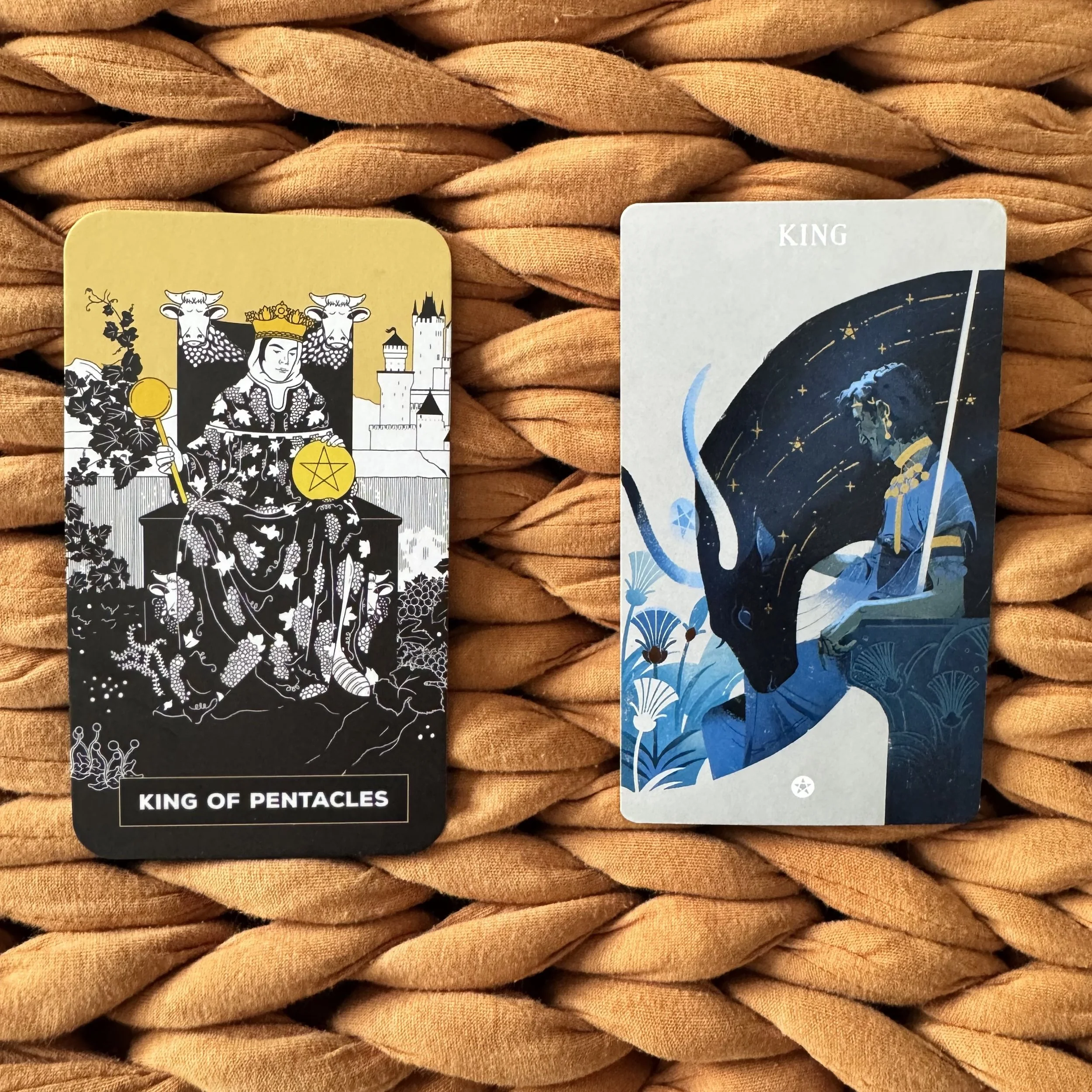 Two tarot cards for the King of Pentacles. On the left, the card shows a person enthroned, holding a scepter and pentacle amid vines. On the right, the person is in shades of blue with a large cow head bending over their throne.