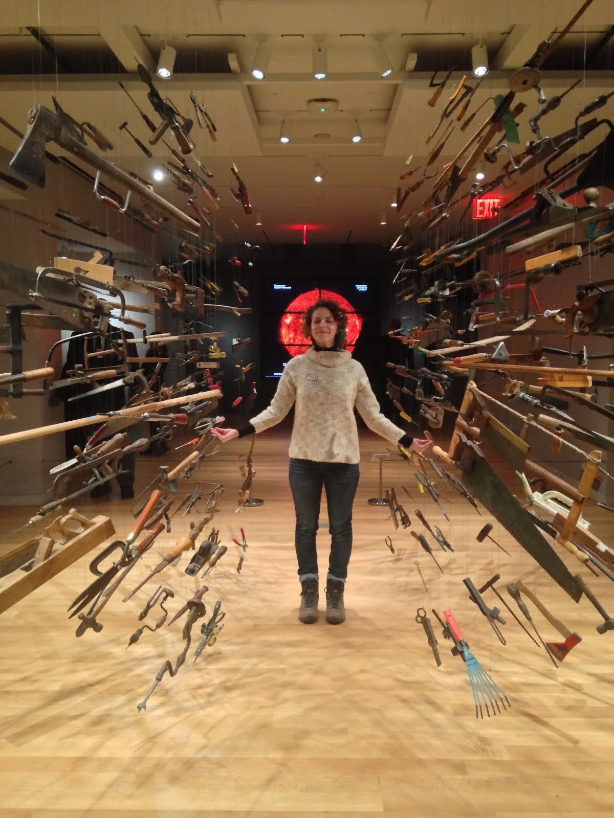 A photo of the author standing straight in the center of an array of old tools suspended from the ceiling in a spherical format that looks like it's spreading out from the center.