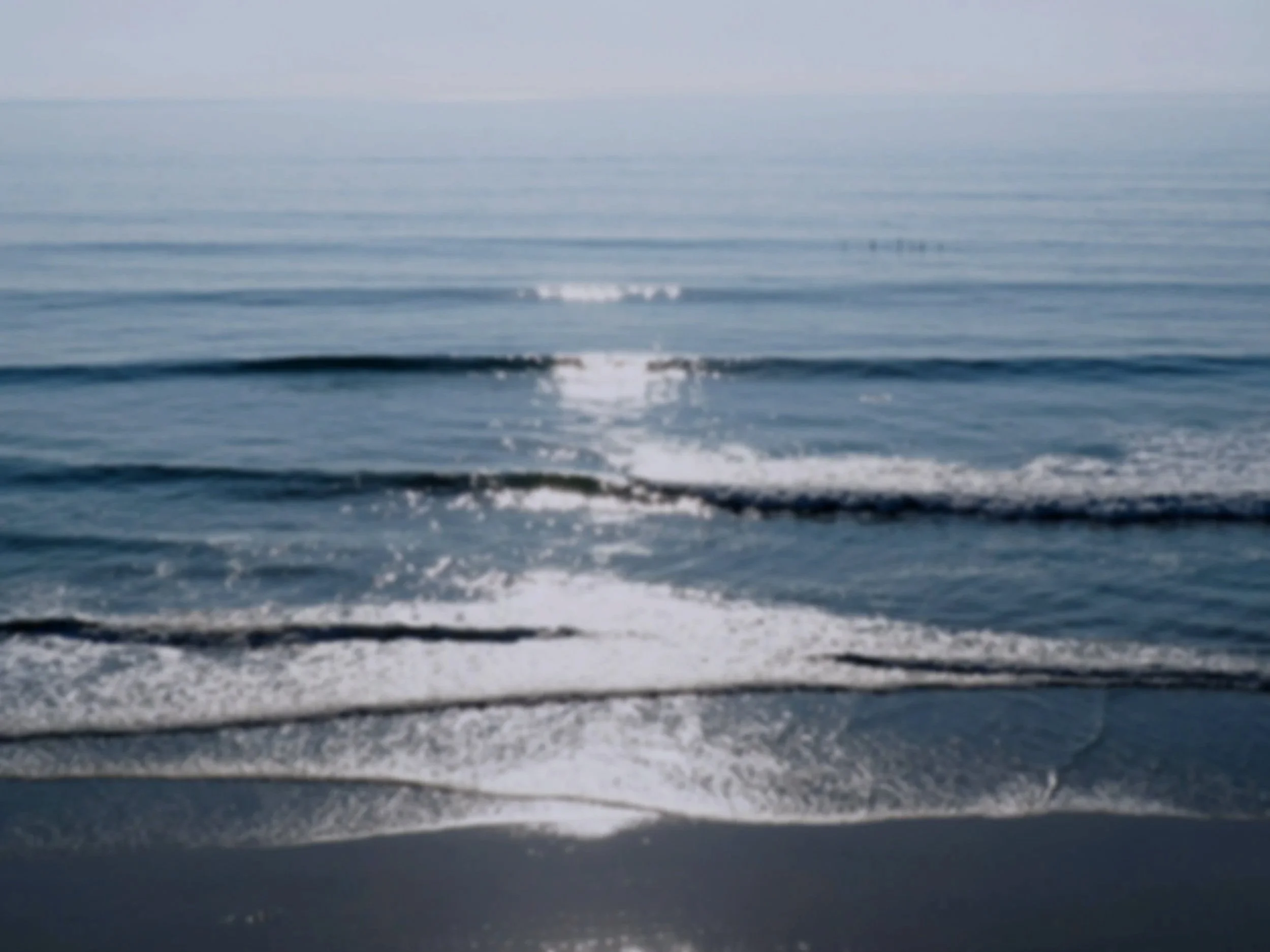 Calm ocean water with gentle waves reflecting sunlight on the surface.