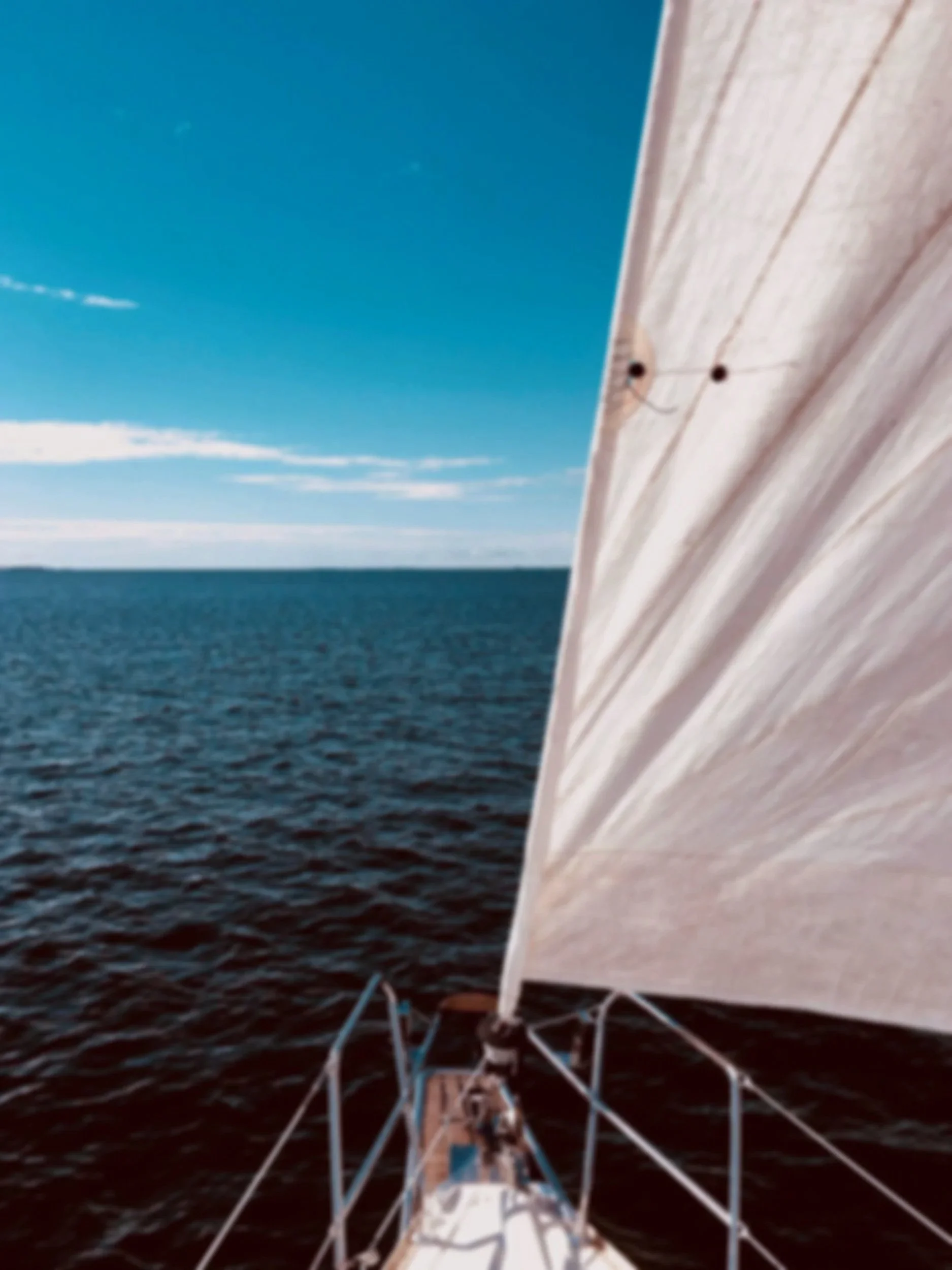 Photo taken from a sailboat showing the deck and white sail with the ocean and blue sky in the background.