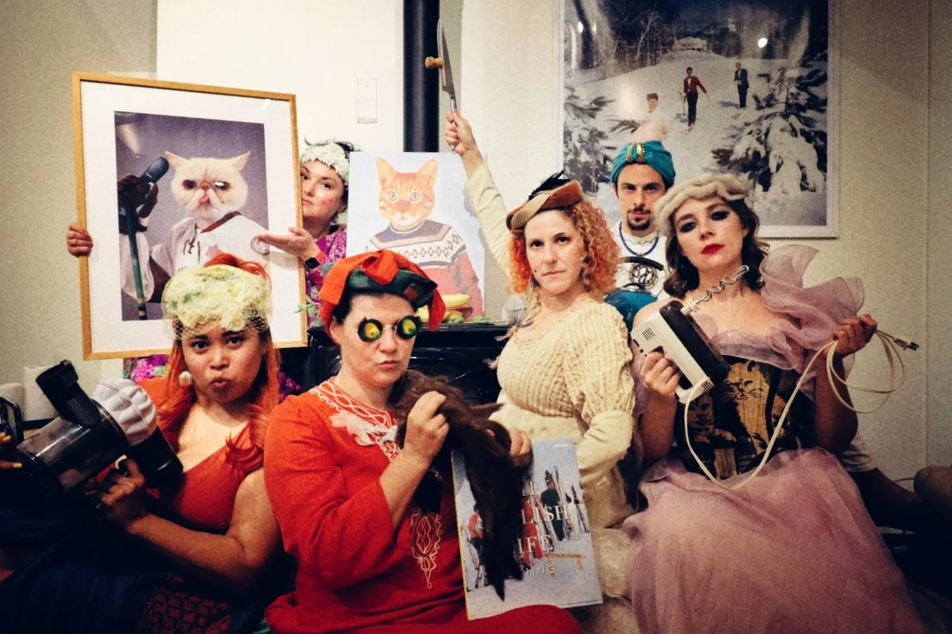 A photograph of 6 people posed in elaborate surrealist costumes, holding various nonsensical props.