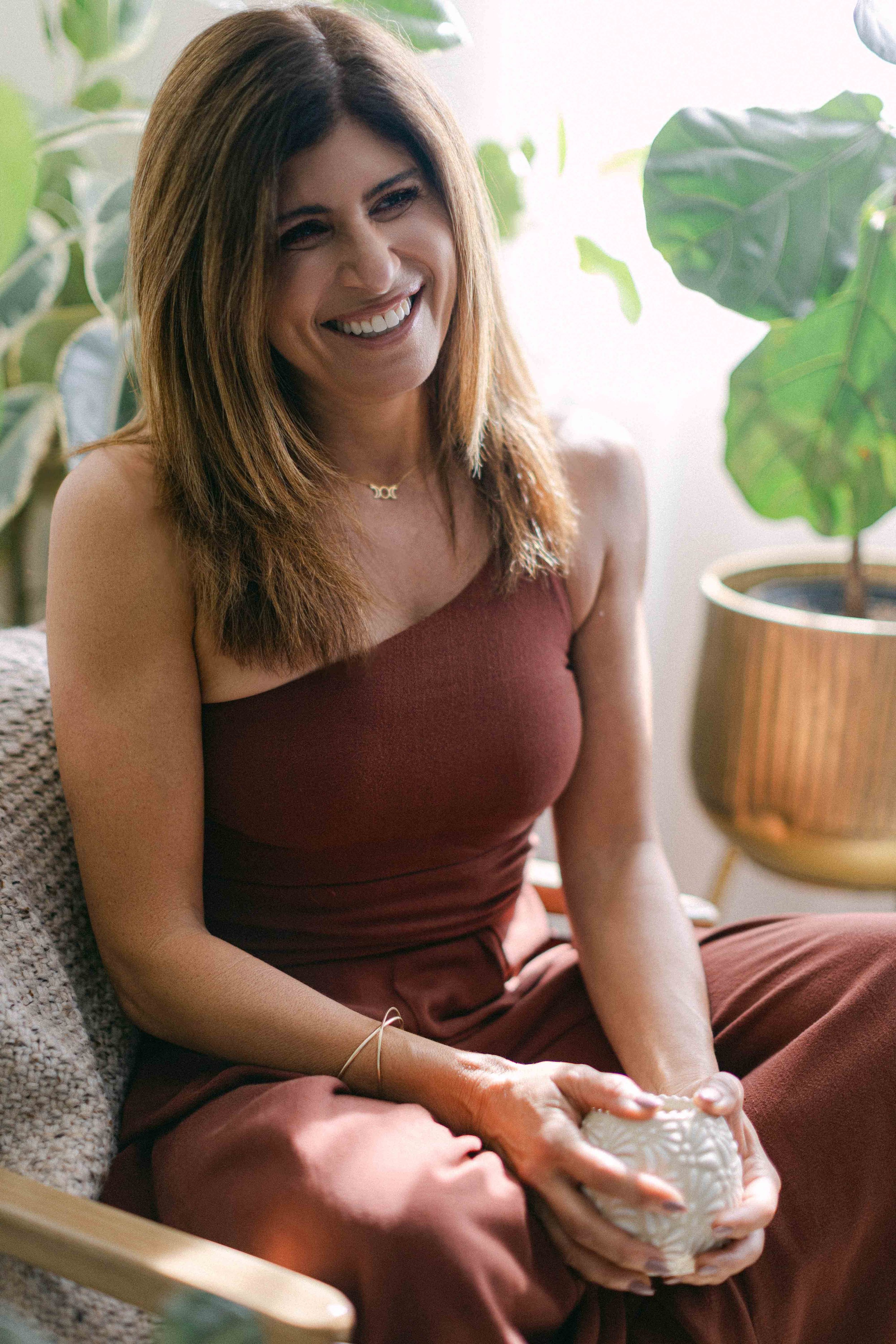 Jennifer, breathwork and Reiki facilitator, smiling warmly in a plant filled healing space.