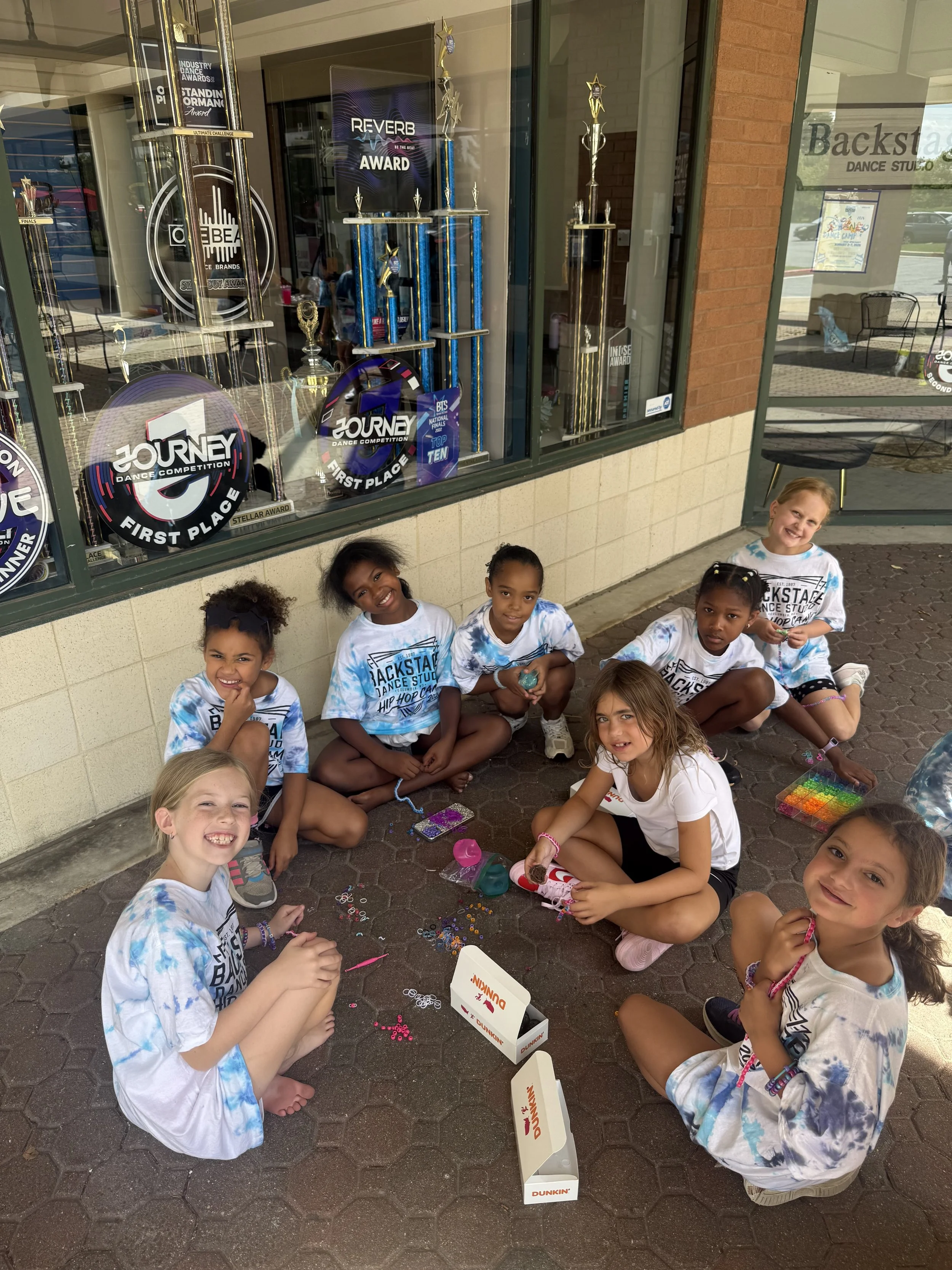Backstage Dance Studio dancers making friendship bracelets together outside during summer dance camp.