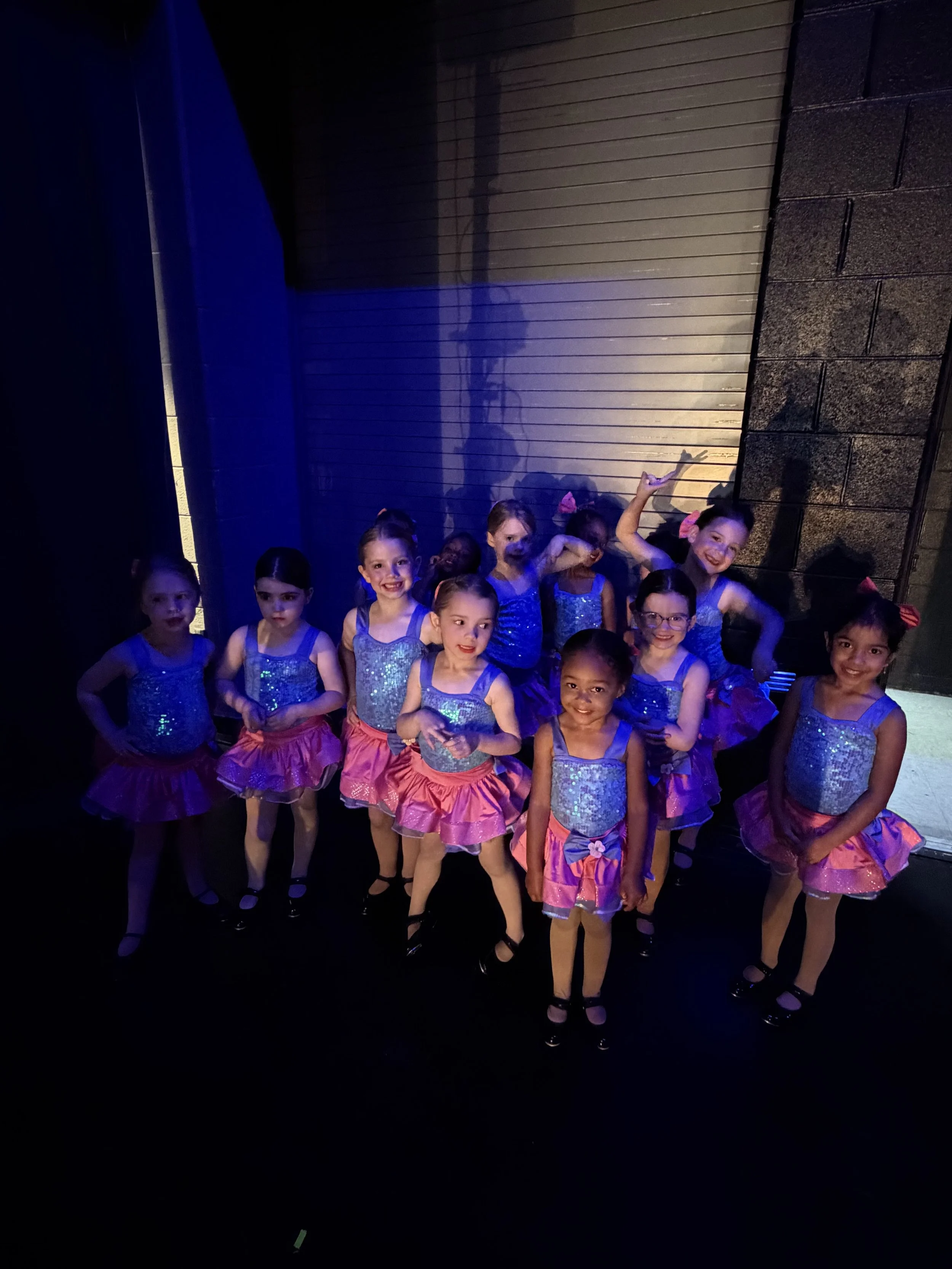 Young Backstage Dance Studio dancers ages 3–5 smiling together backstage during the annual dance recital.