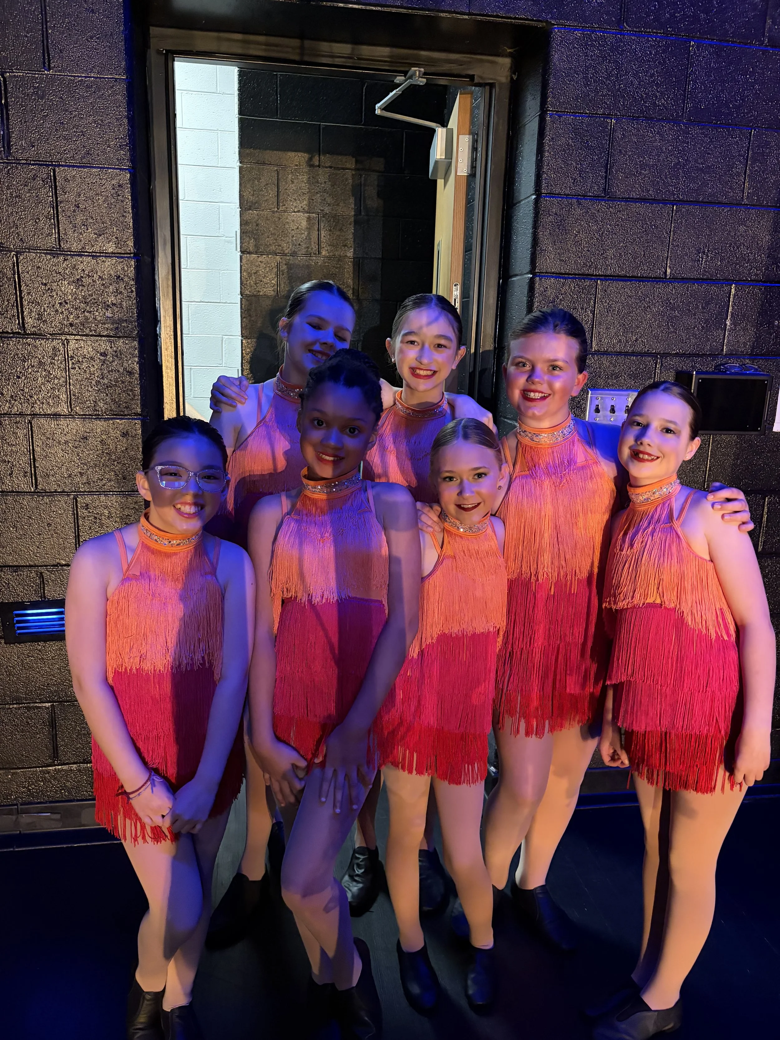 Backstage Dance Studio dancers smiling together backstage during the annual dance recital.