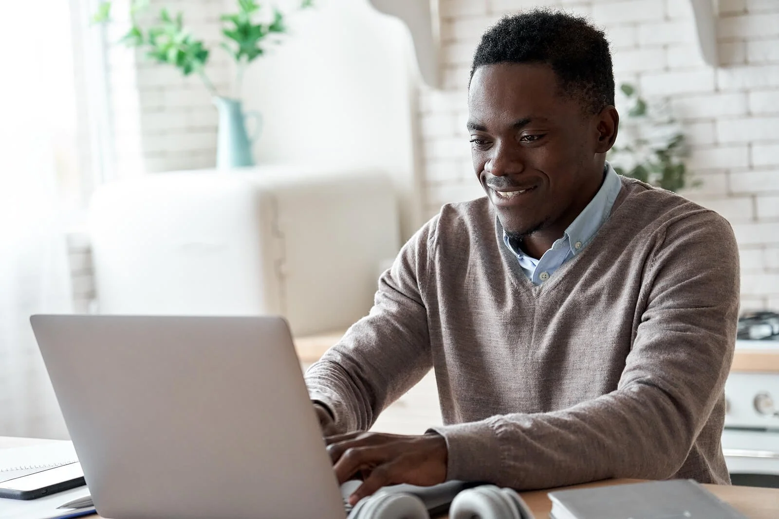 Smiling man in a brown sweater working on a laptop at a bright home workspace with white brick walls. When your bidding strategy matches where your practice is in its growth, Google Ads for Therapists starts delivering the leads you actually need.