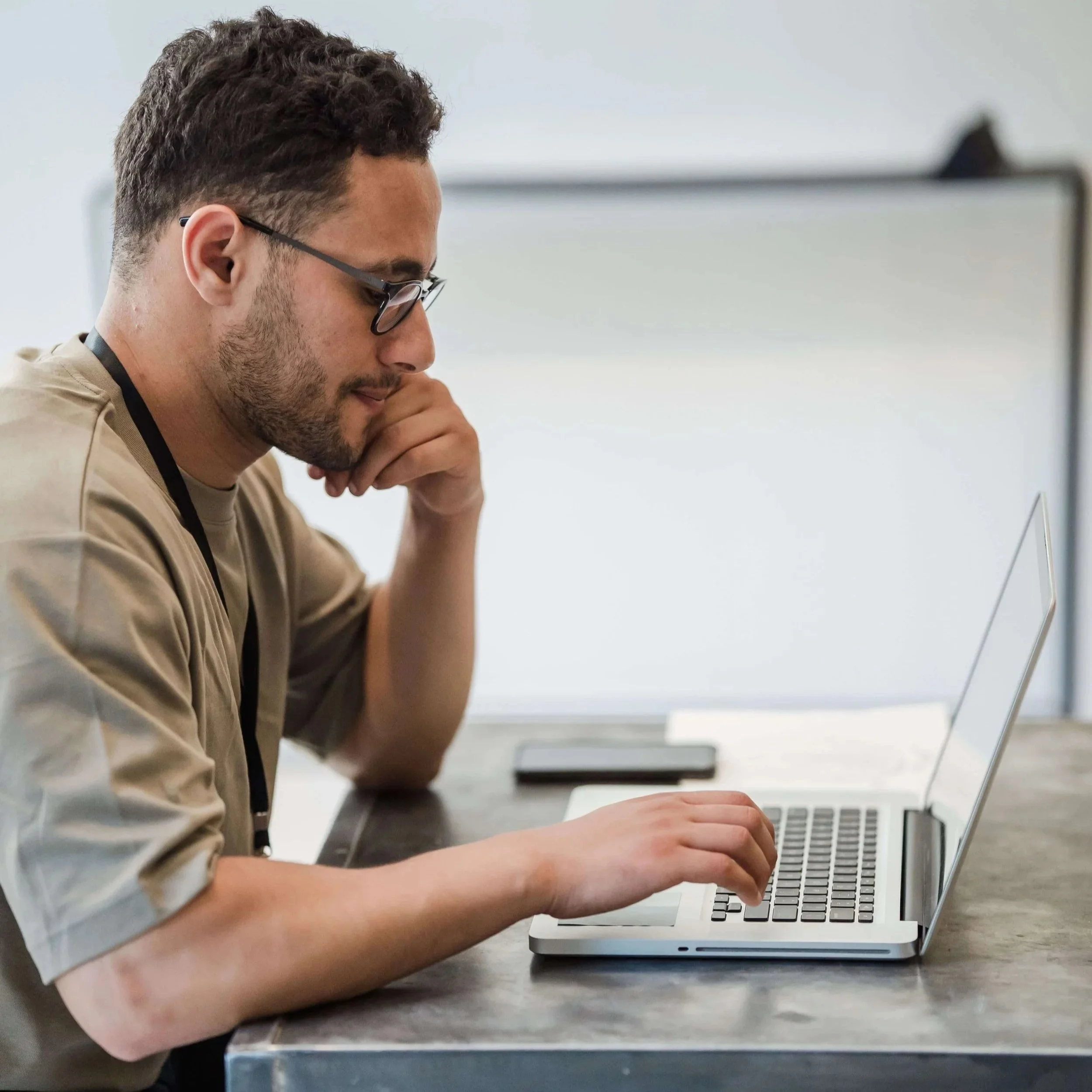 Young man with glasses and a beard sitting at a metal desk, focusing on a laptop. If your Google Ads for Therapists campaign is getting clicks but no calls, misaligned targeting could be sending the wrong people to your site.