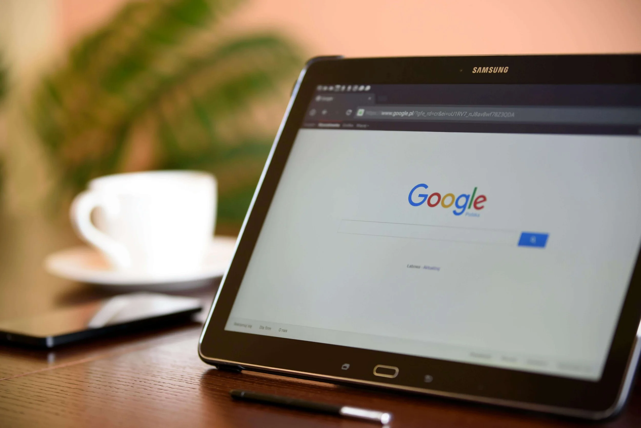 Samsung tablet displaying Google homepage on wooden desk with blurred coffee cup in background. Optimize your website to lower costs and improve results from your Google Ads for Therapists campaigns.