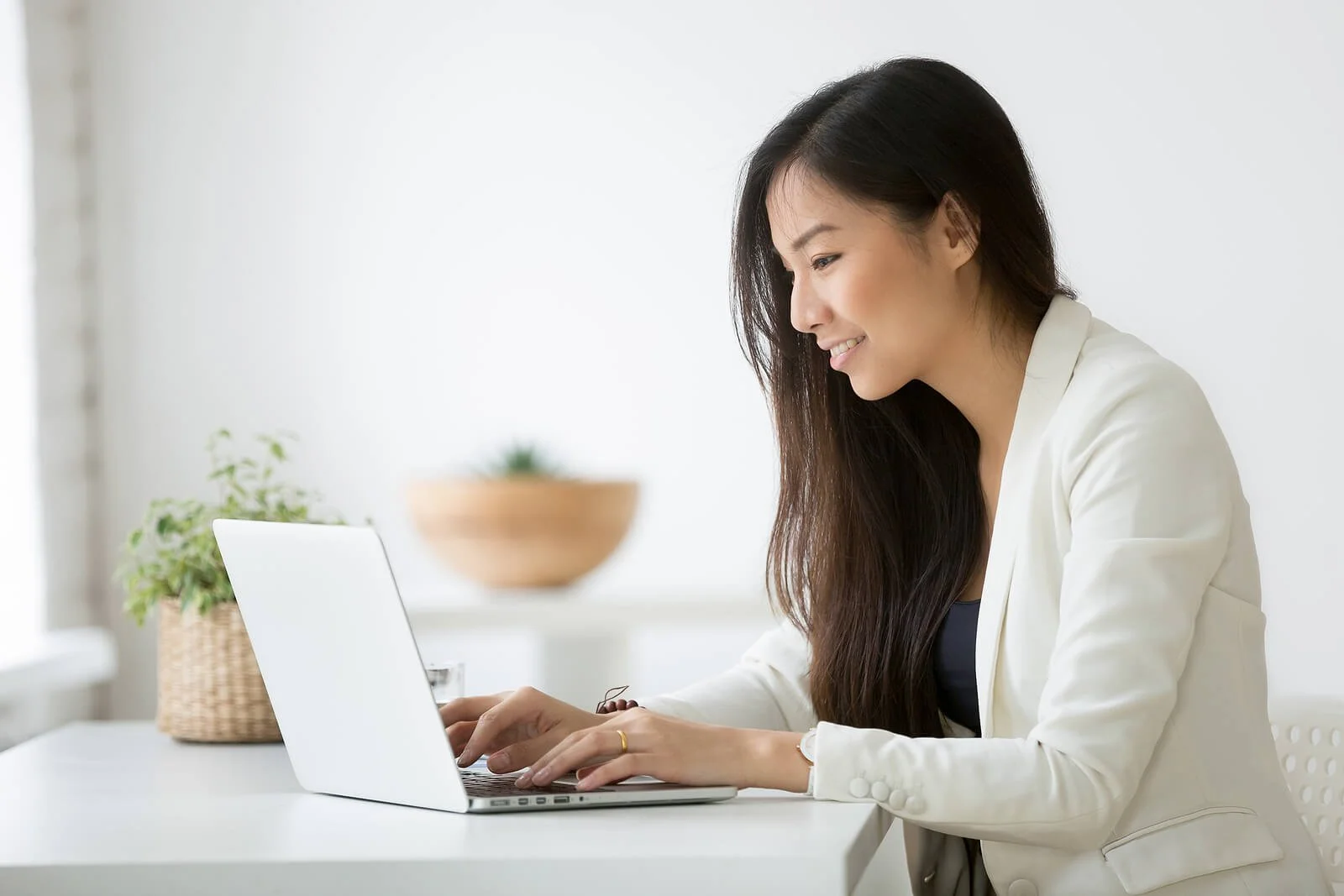 Woman in white blazer working on laptop at desk with plant in minimalist office. Strategic patience during the learning phase ensures Google Ads for Therapists builds sustainable lead generation.