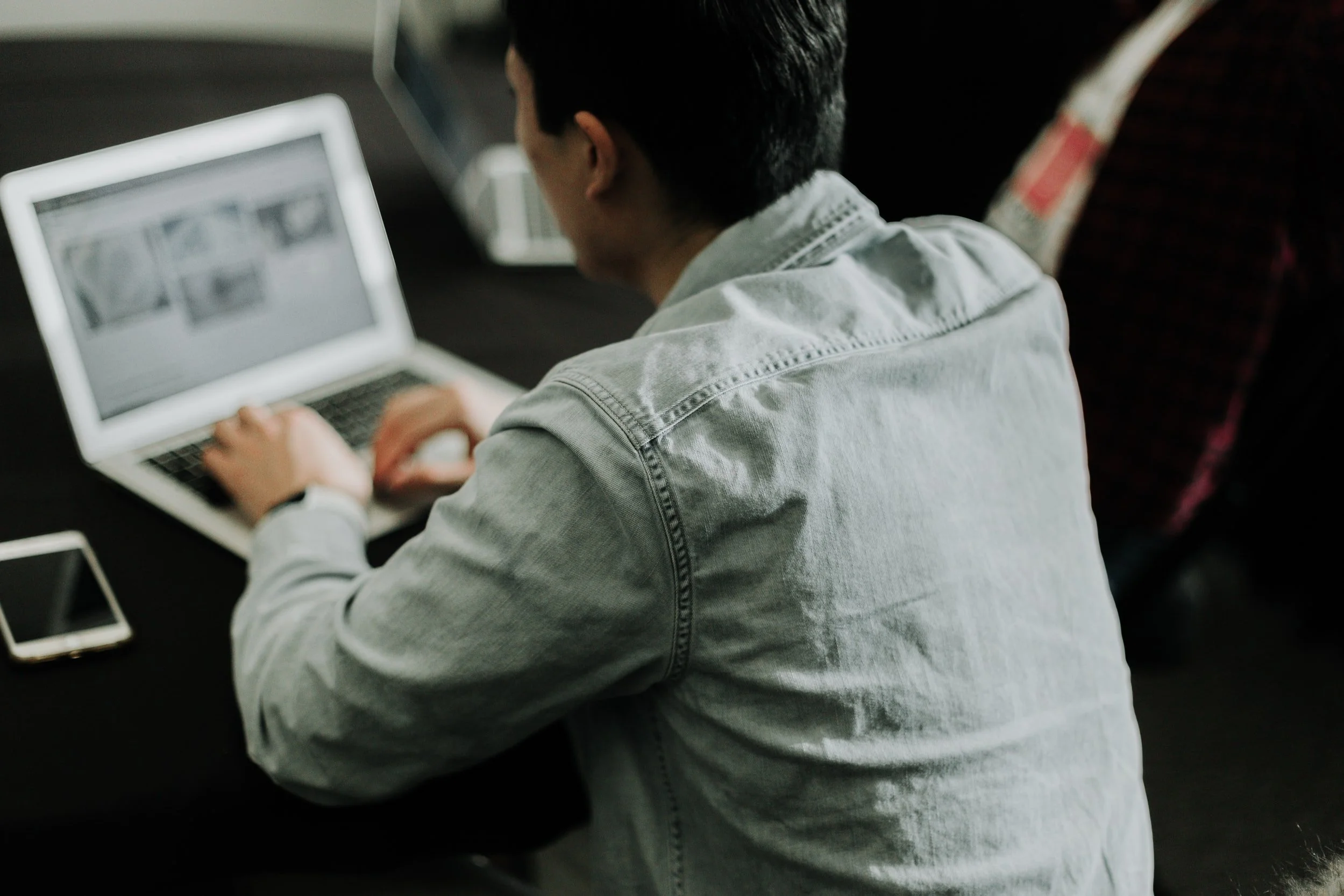 Man sitting at a table using a laptop, with a smartphone nearby.