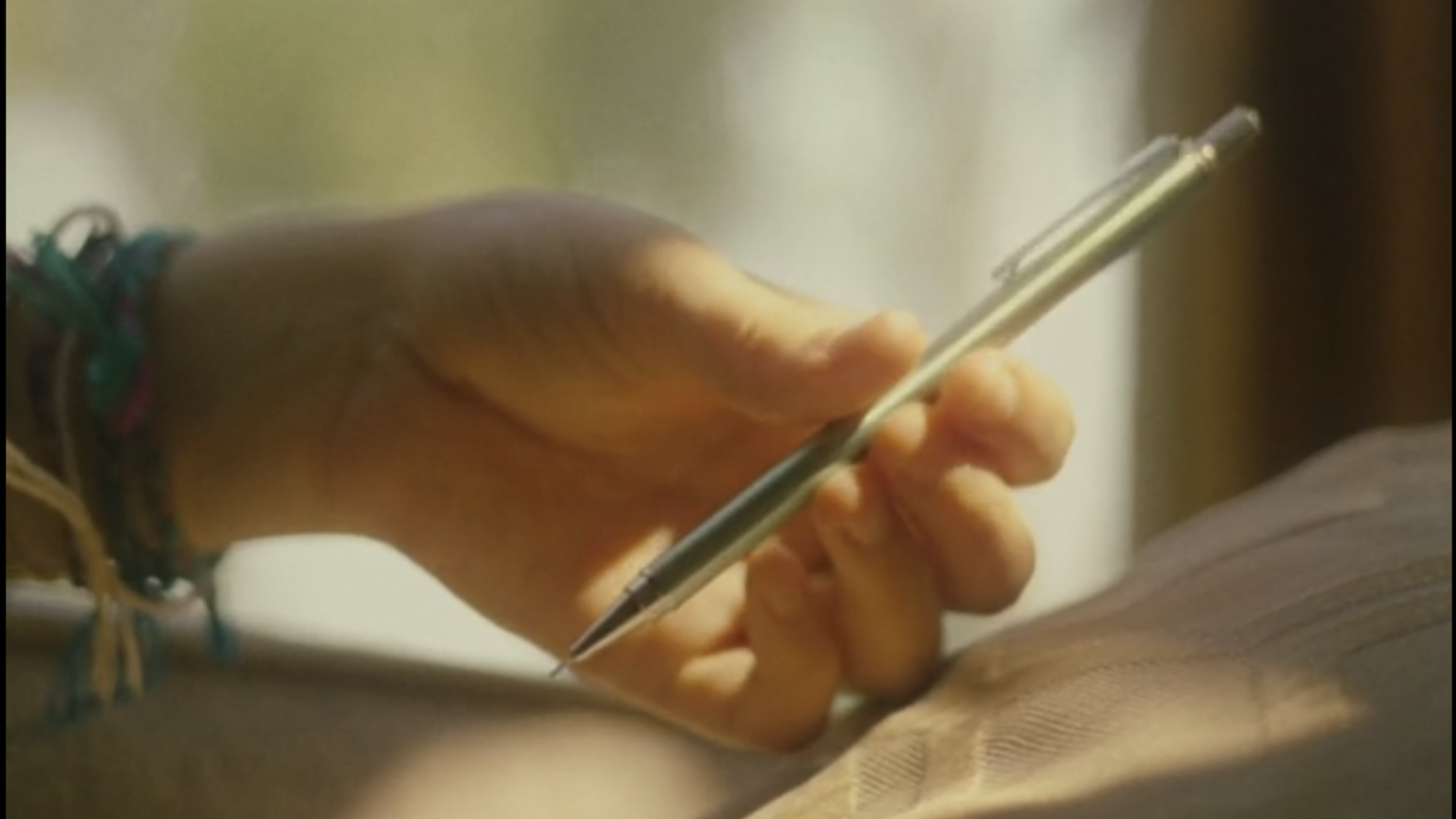 Une main tenant un stylo argenté, écrivant sur une surface en tissu ou en papier.