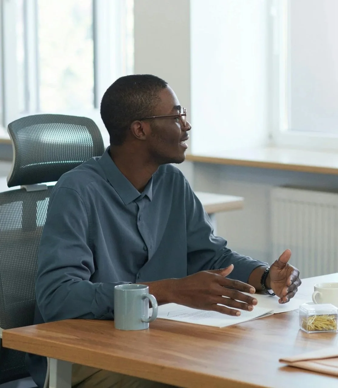 A confident Black man career coach coaching a colleague at a wooden table in an ergonomic office chair.